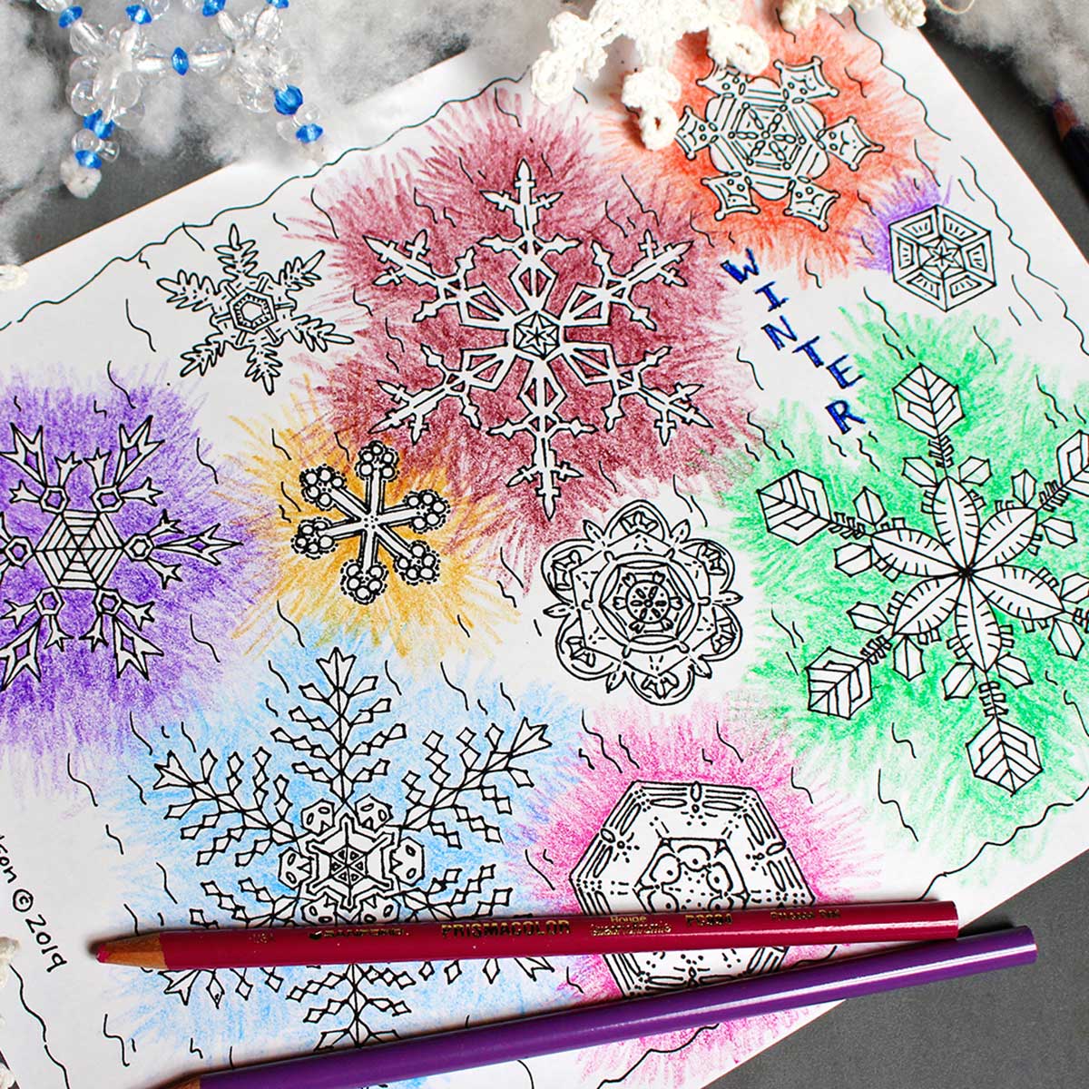 Snowflake coloring page colored with bursts of colored pencil around snowflake shapes.
