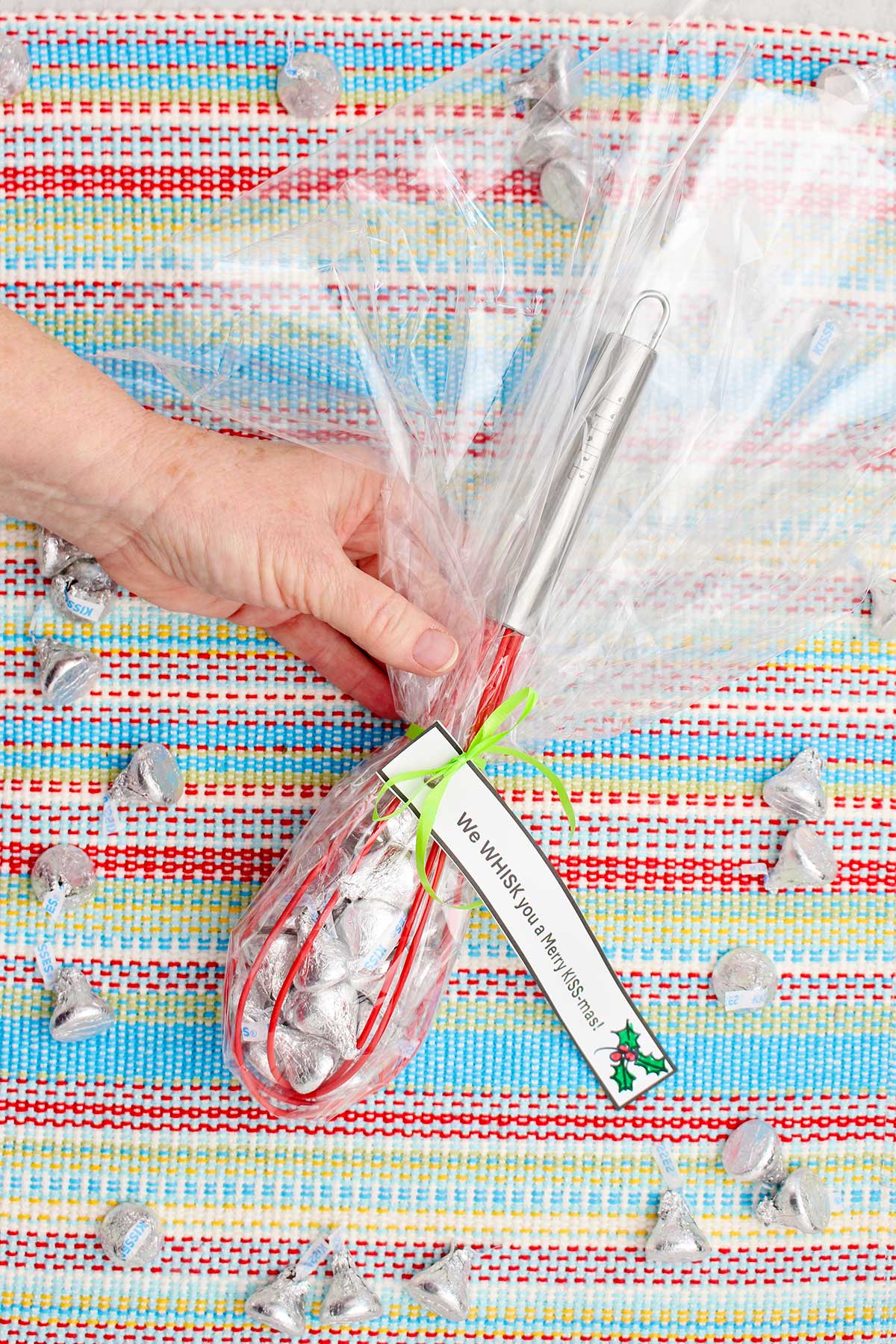 A person holding a wrapped and completed whisk candy gift wrapped in cellophane with a little note tied on.