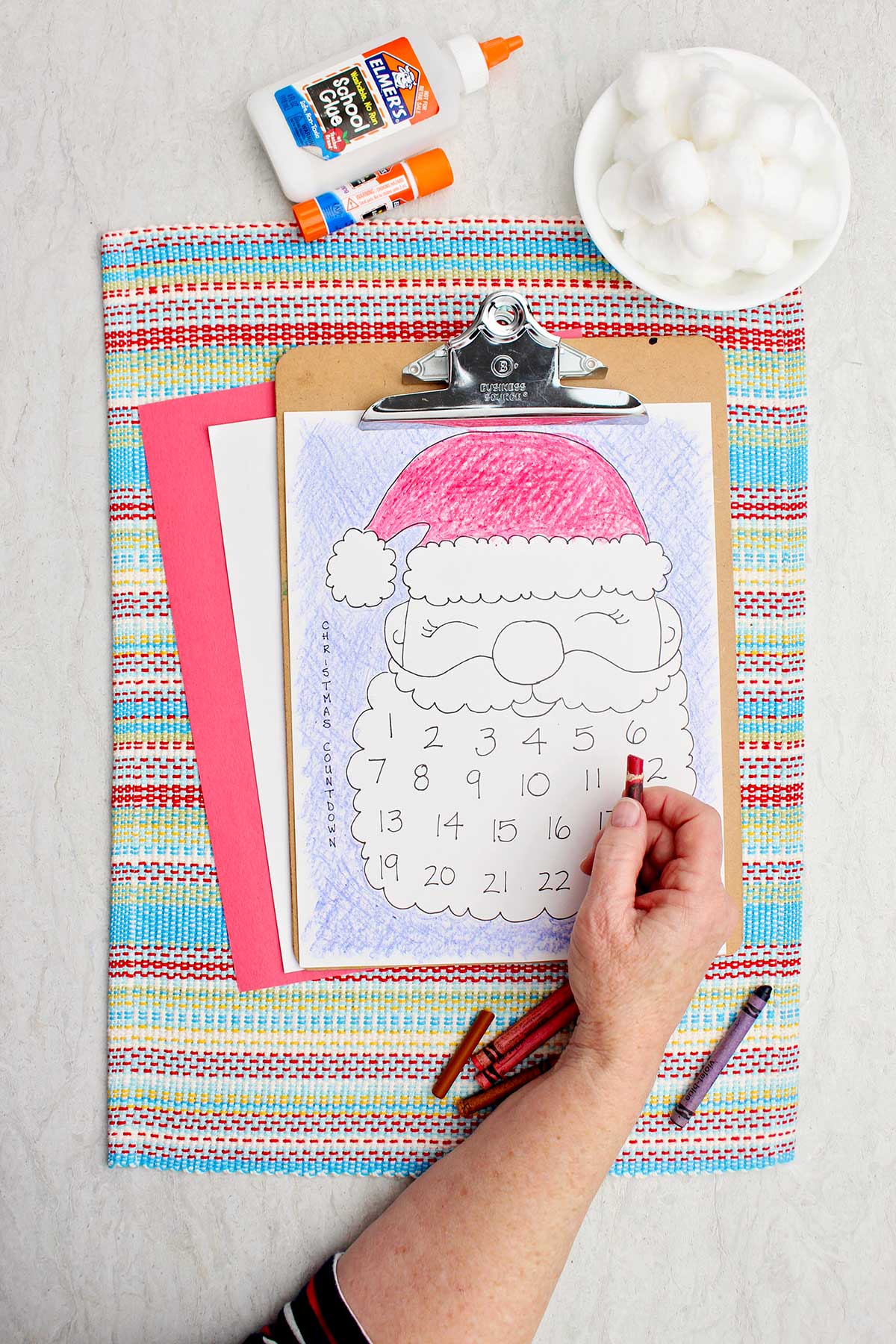 A person coloring Santa's hat red in the calendar printout.