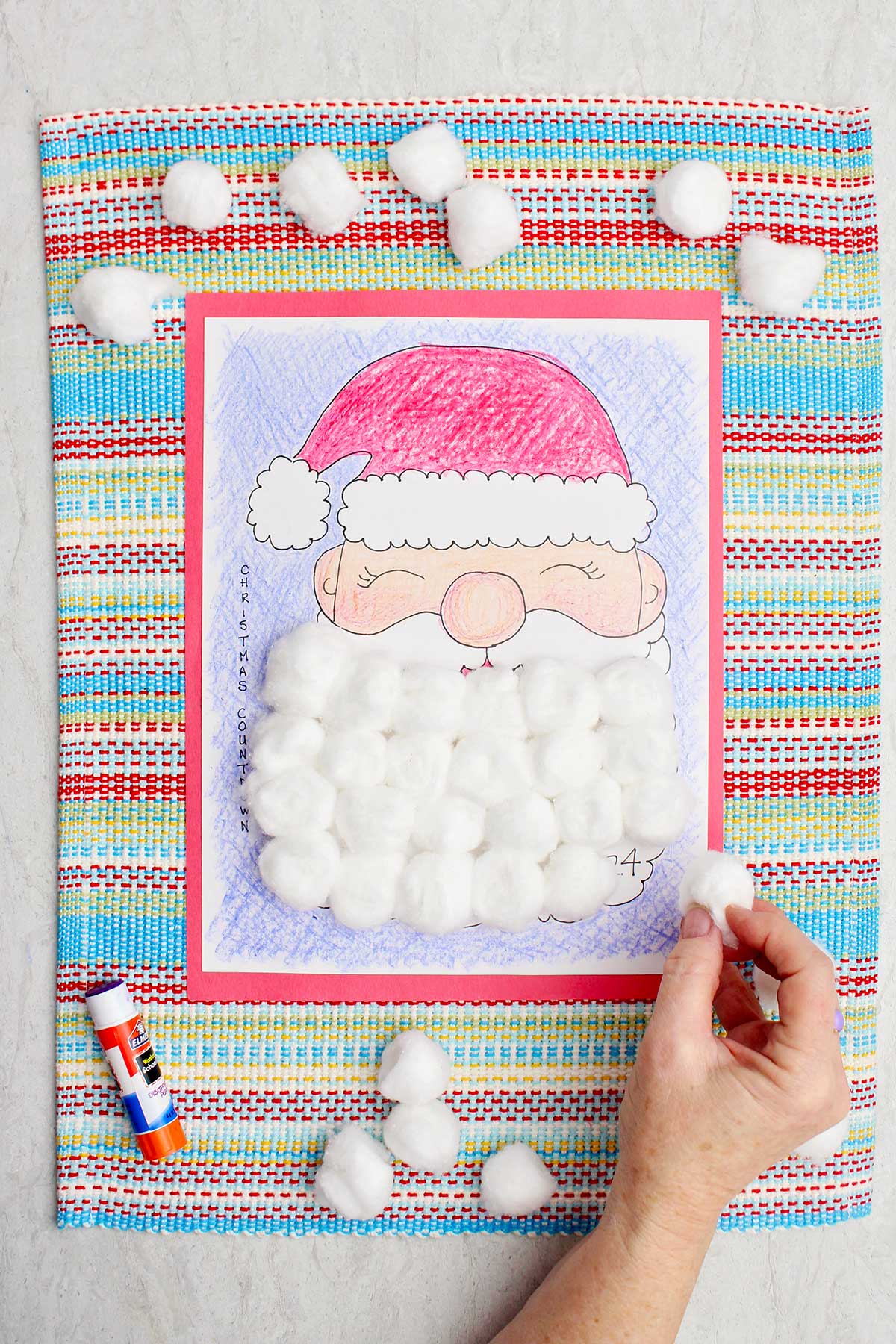 A person putting a cotton ball on a day on Santa's beard in the calendar countdown.
