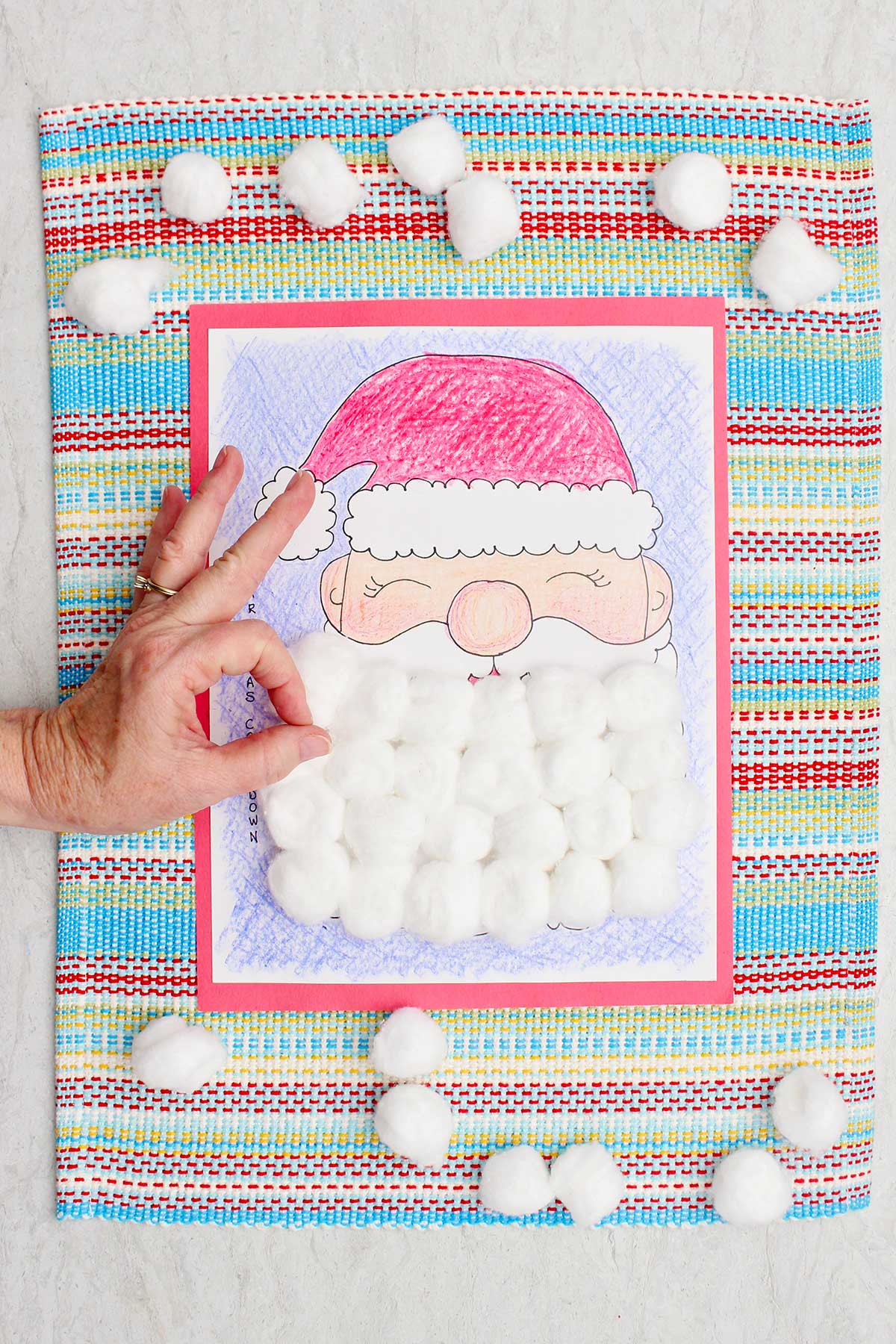 A completed Christmas countdown calendar colored with crayon and Santa's beard covered with cotton balls and a person making the "okay" sign.
