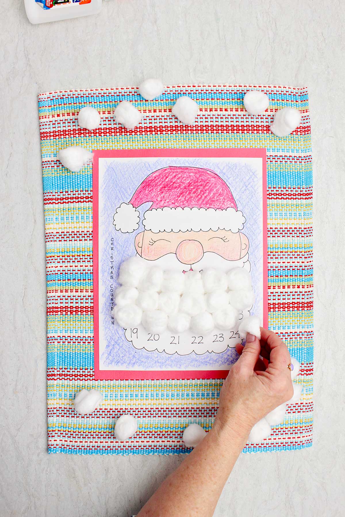 A person putting a cotton ball on a day on Santa's beard in the calendar countdown.