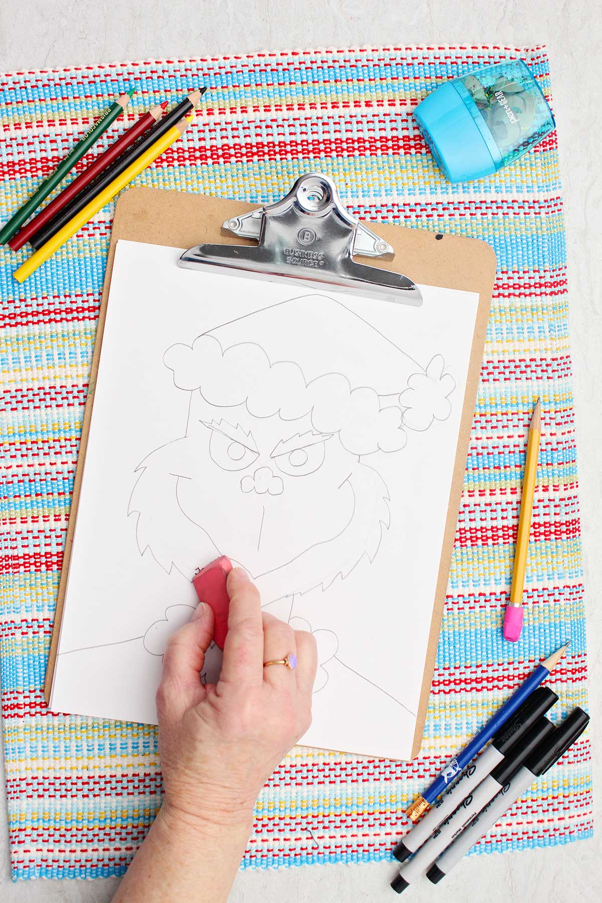 Person cleaning up some lines with a pink eraser on their Grinch sketch.
