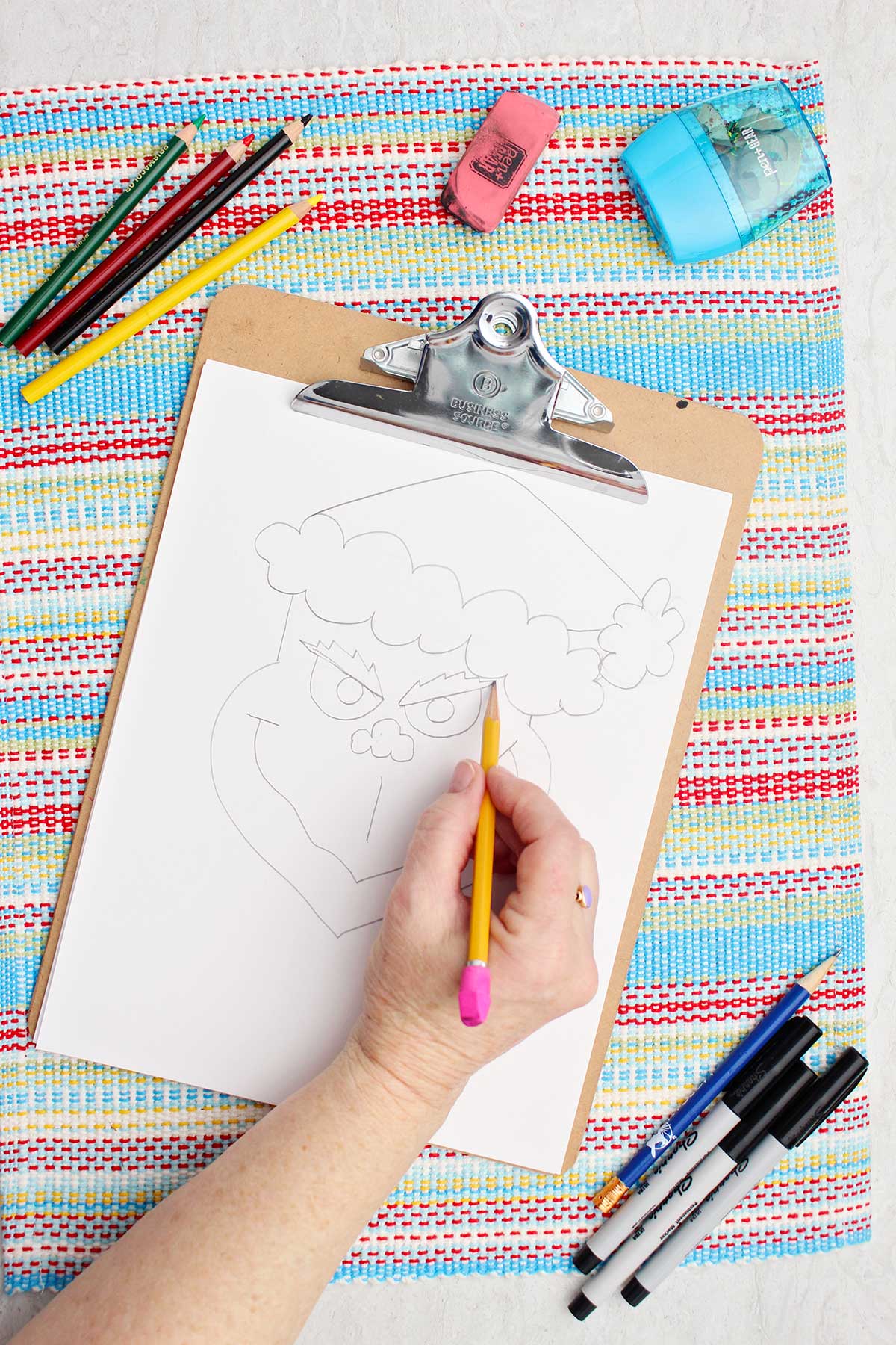 Person drawing eyebrows on Grinch sketch.