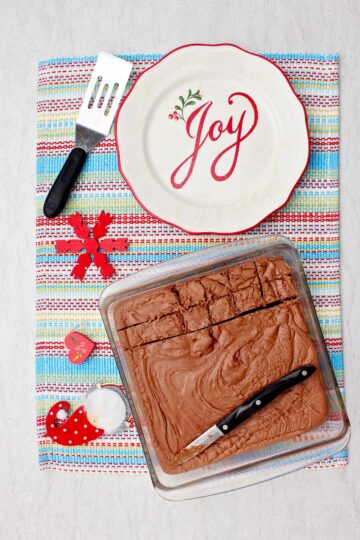 Finished fudge in glass baking pan on colorful placemat with festive plate and spatula near by.