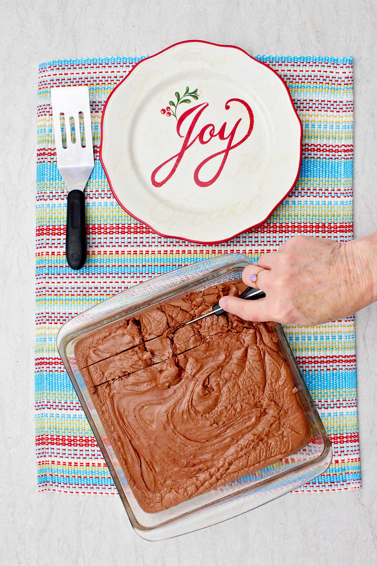 Person cutting into final pan of fudge on colorful placemat with festive plate near by.