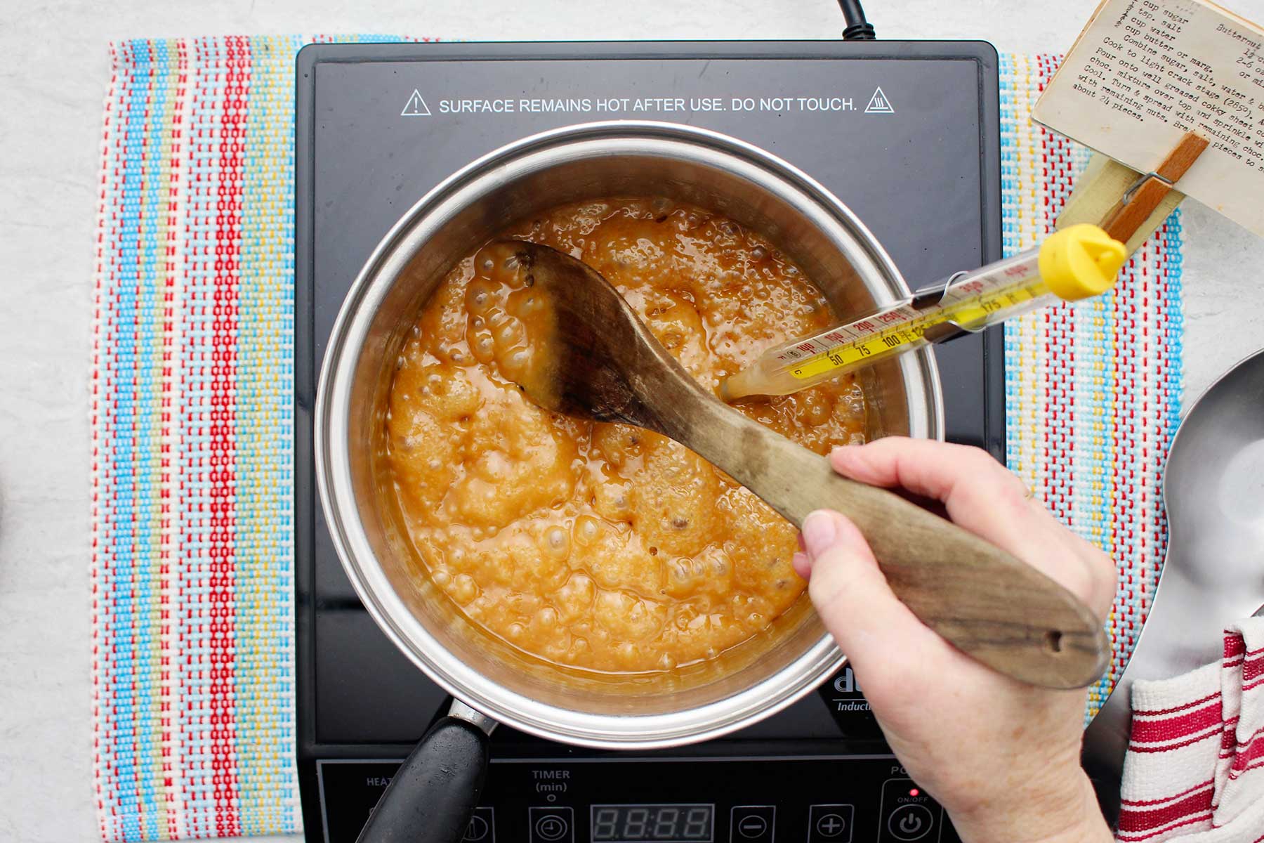 Person stirring darkening bubbling toffee mixture in a saucepan.