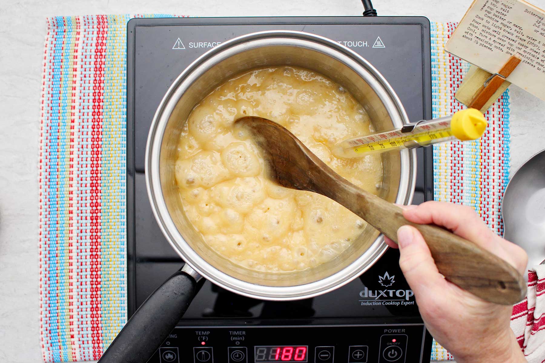 Person stirring bubbling toffee mixture in a saucepan.