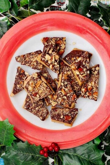 A red rimmed plate of toffee surrounded by festive ivy.