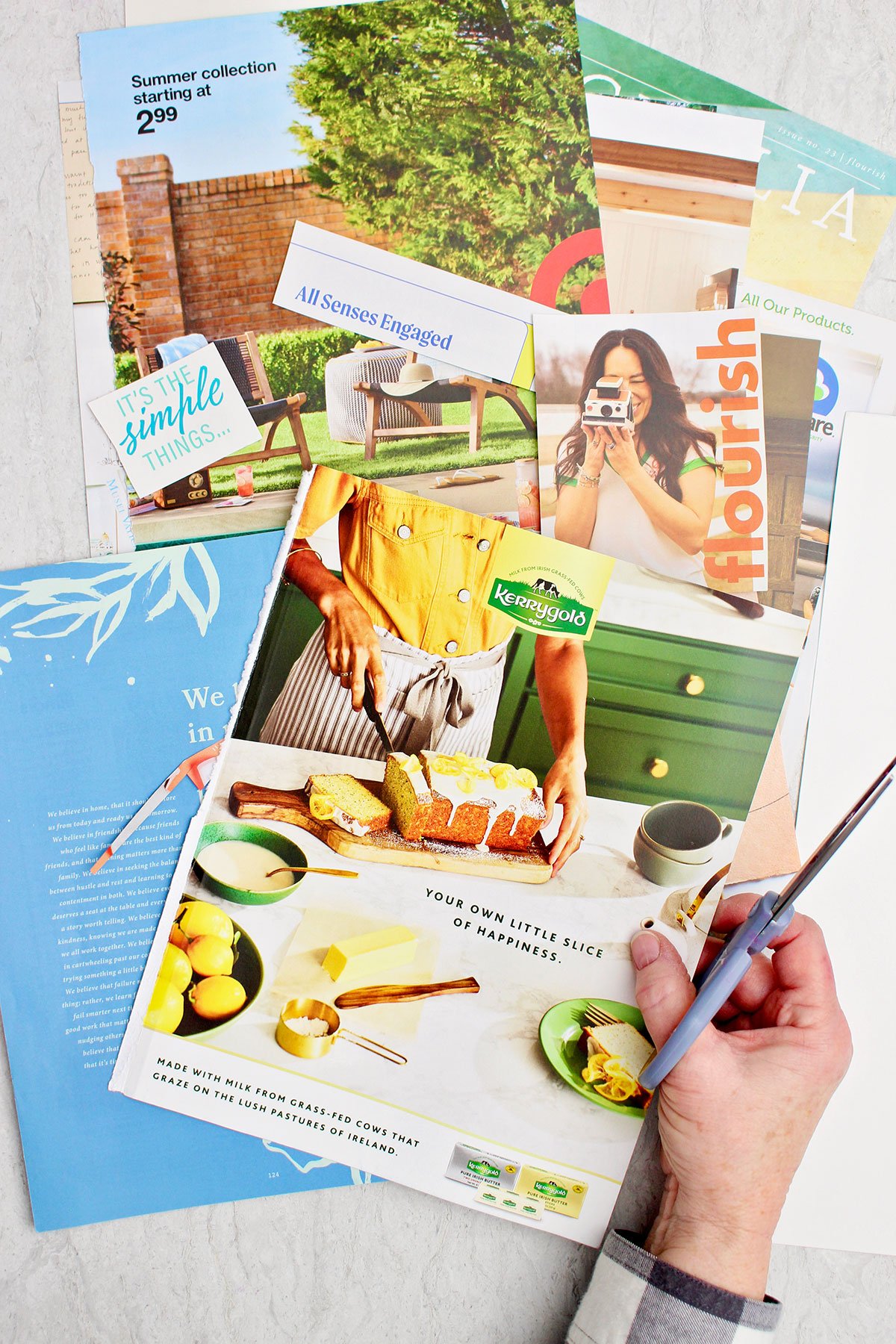 A person holding a pair of scissors and some bright colored magazine cut outs for a vision board.