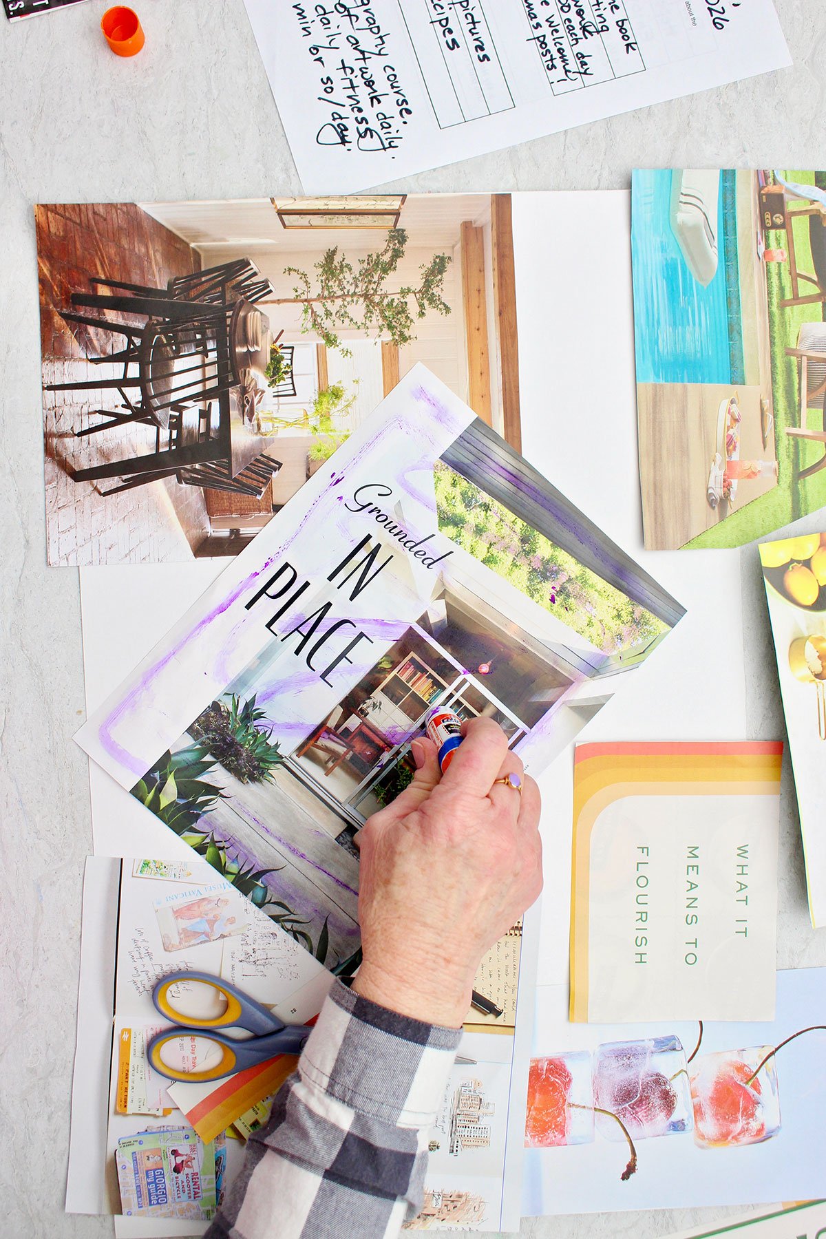 A person gluing a large magazine page on their vision board with a purple glue stick.