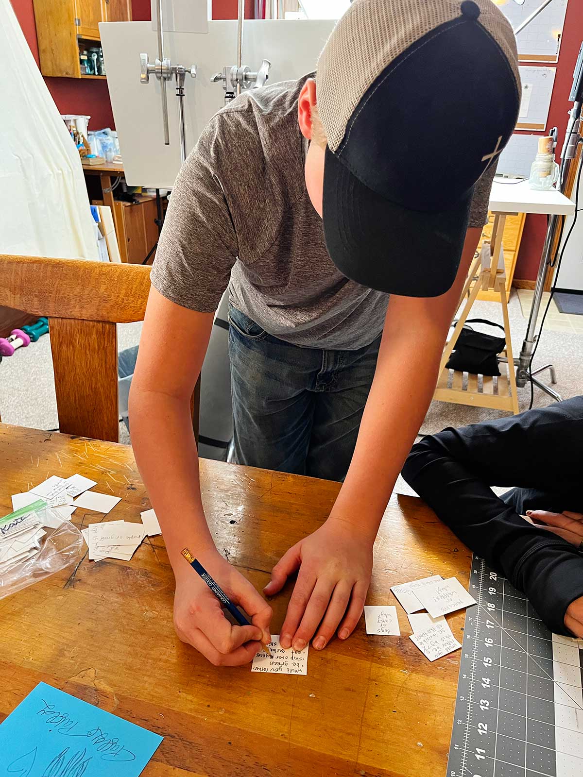 A boy in a baseball cap writing a Would You Rather question on a piece of paper.