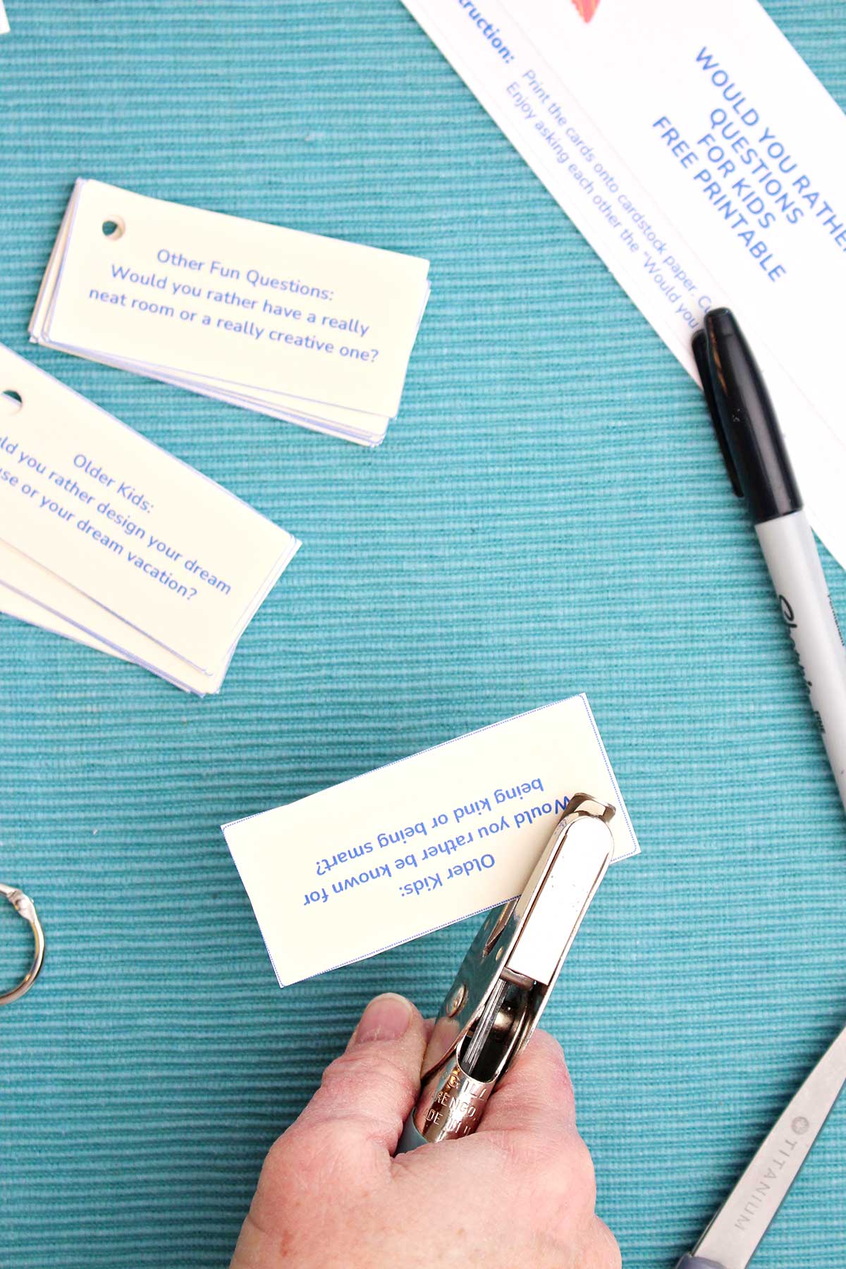 A person punching a hole in the corner of a Would You Rather Question on a small piece of paper.