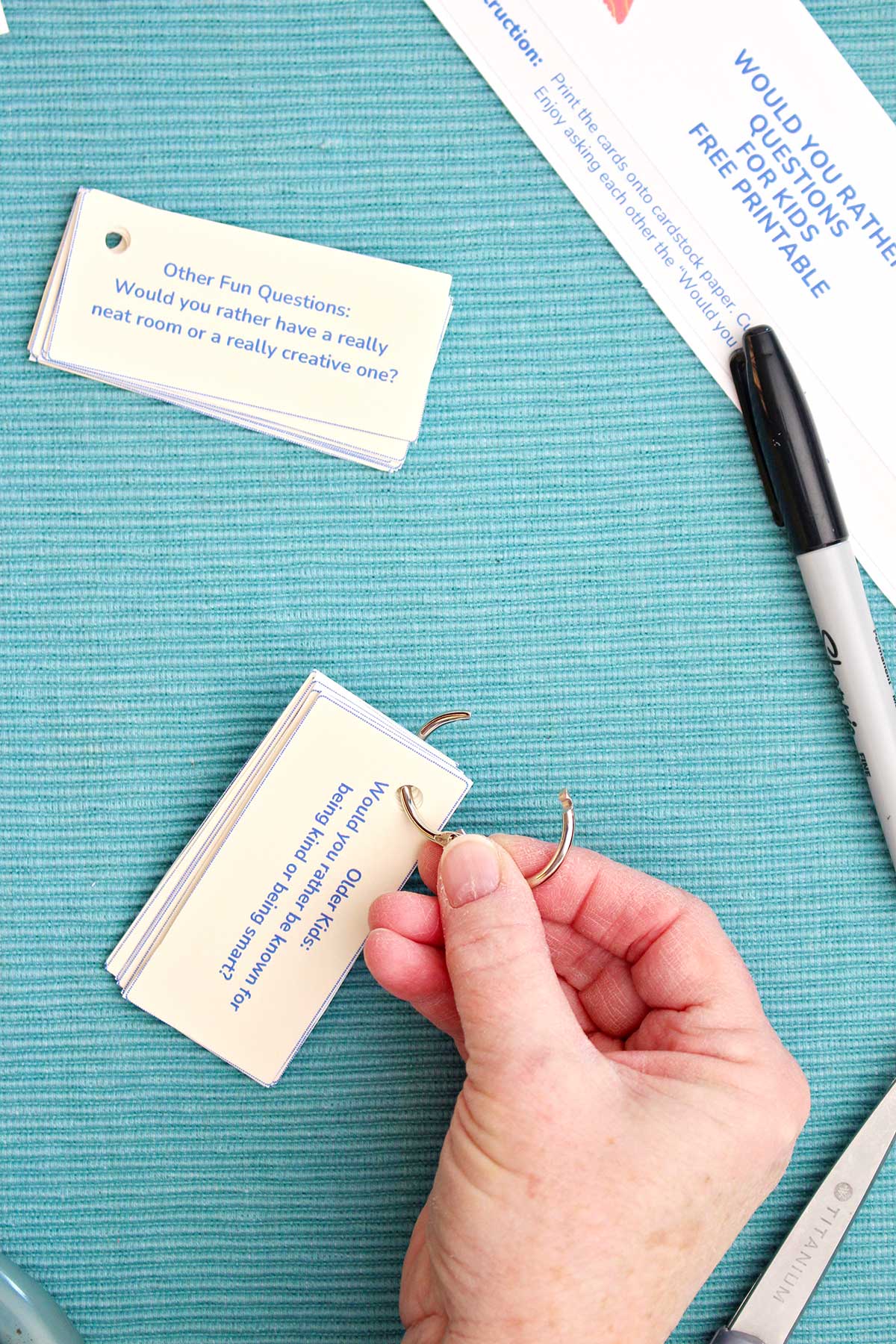 A person adding a ring to a stack of Would You Rather Questions next to a marker.