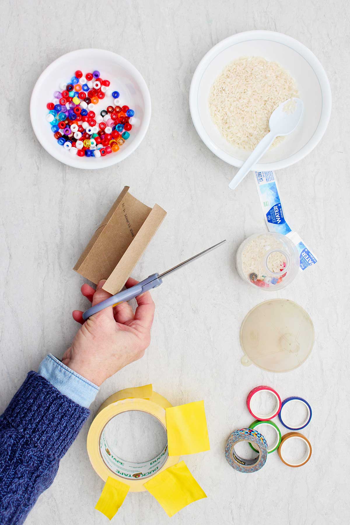 Person cutting a toilet paper roll in half long ways to make a maraca handle.
