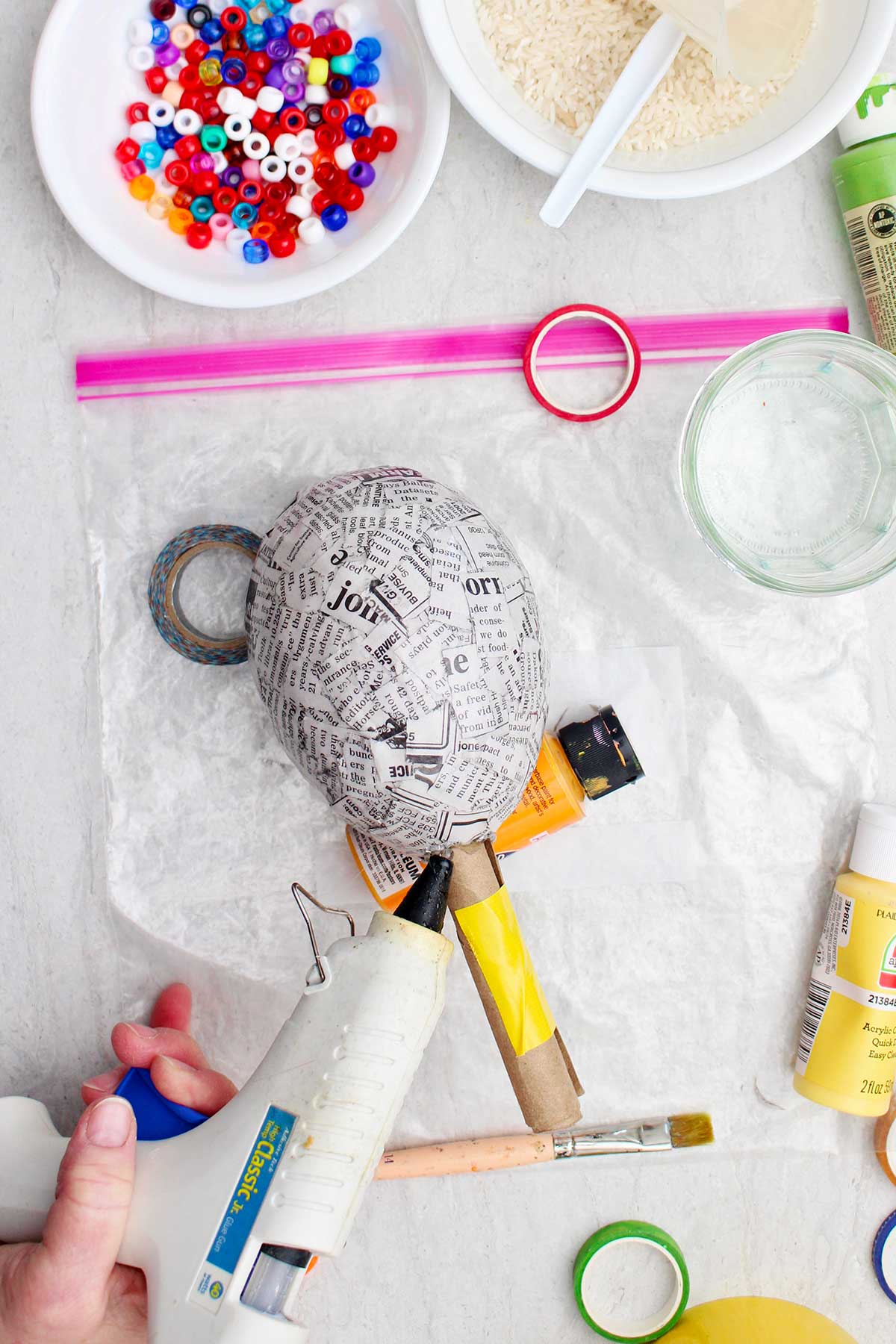 Person using hot glue to secure the bottom of the maraca to the handle with other supplies near by.