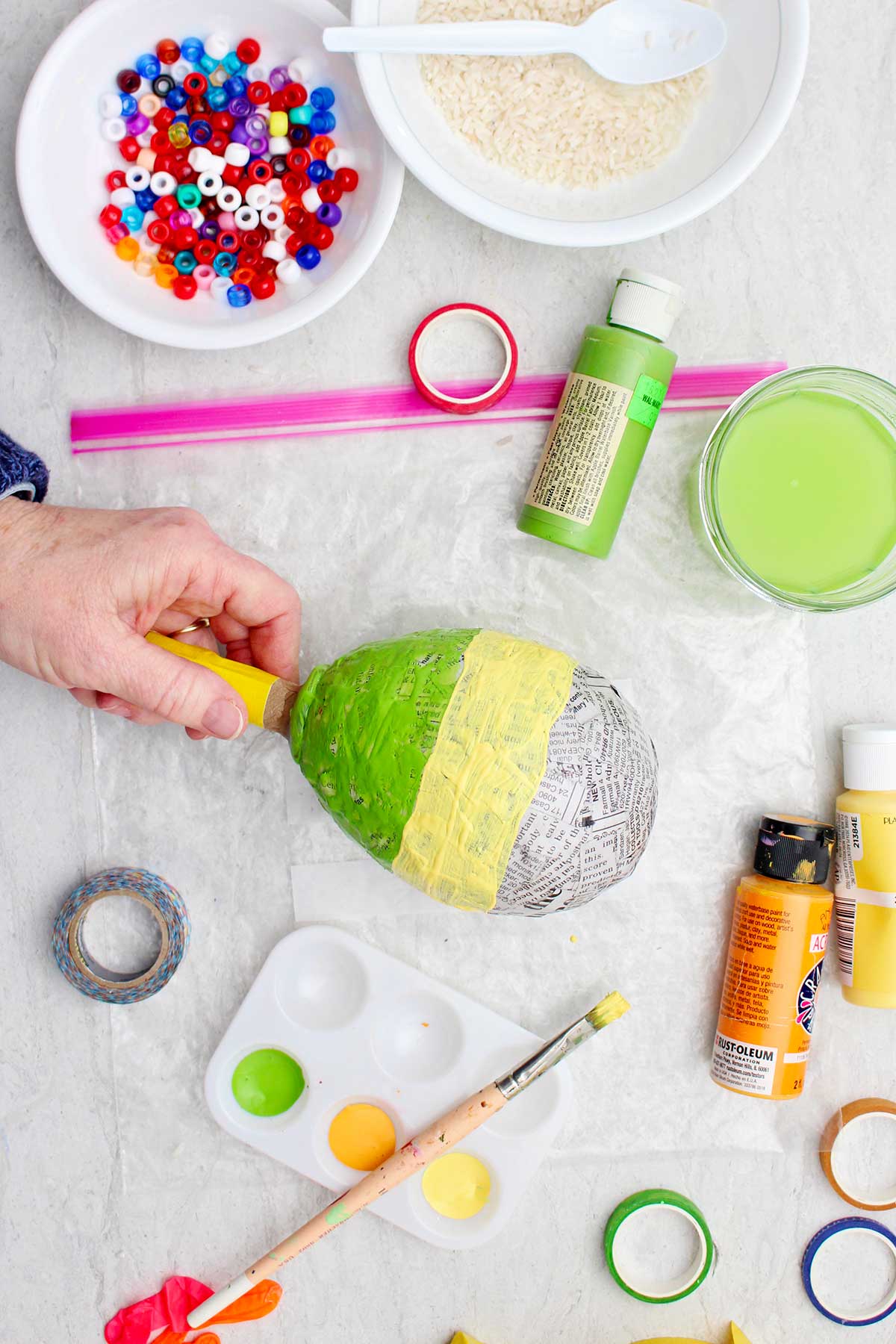 Person holding a half painted newspaper maraca with supplies near by.