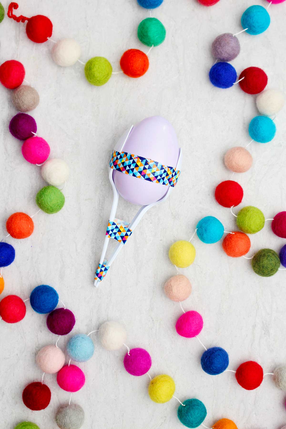 Lavender plastic egg maraca with spoons and washi tape with colorful pom poms near by.