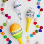 Three different completed maracas with colorful pom poms near by.