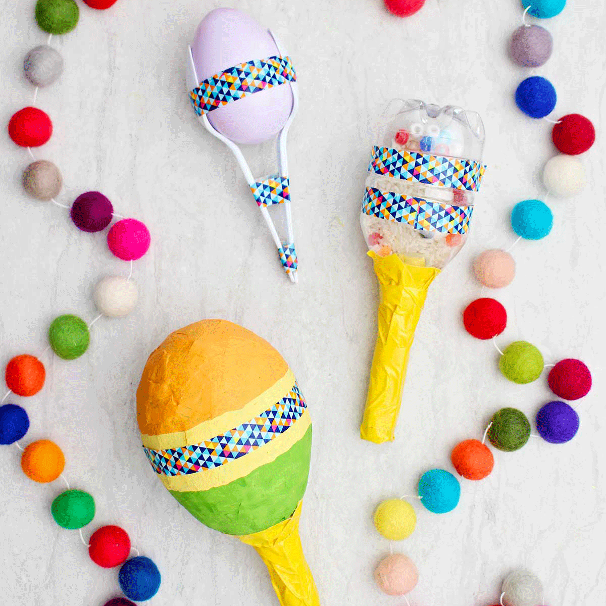 Three different completed maracas with colorful pom poms near by.