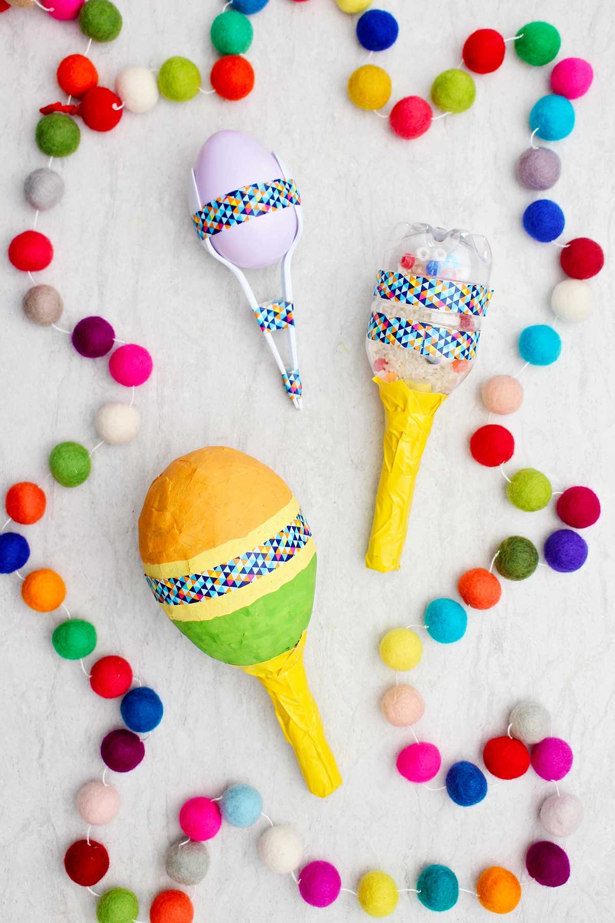 Three different completed maracas with colorful pom poms near by.