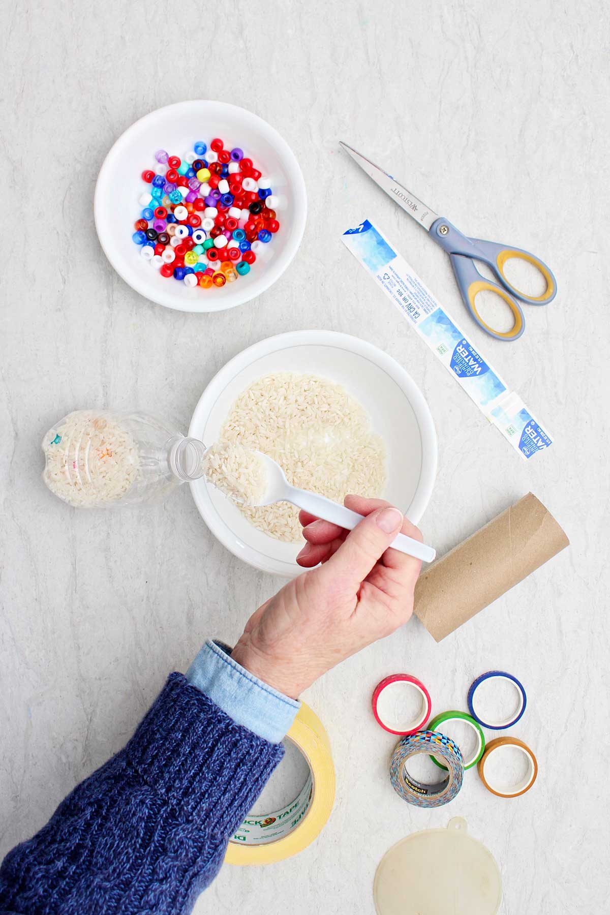 Person filling an empty water bottle with dried rice and beads.