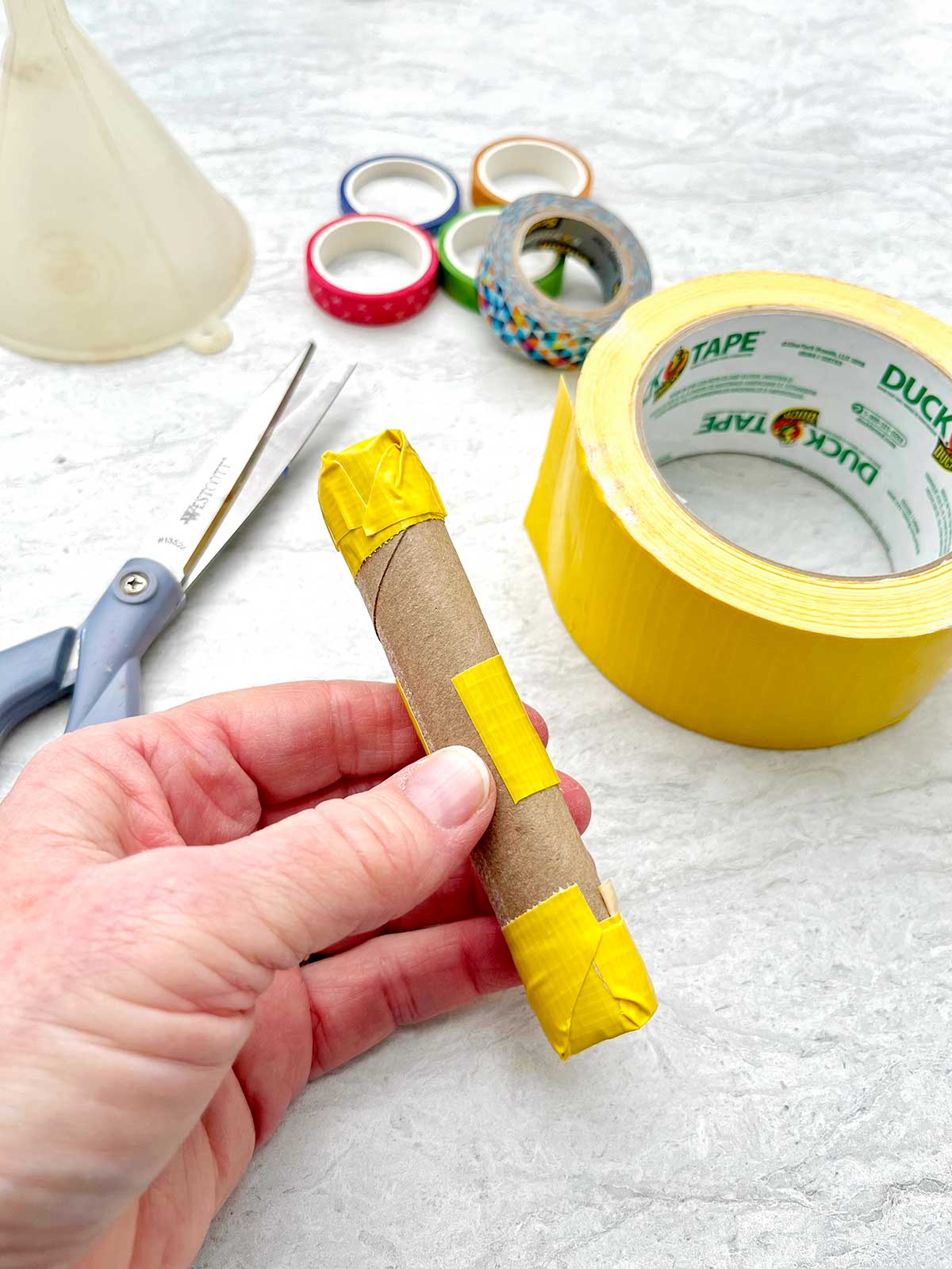 Person showing how to secure a toilet paper roll together to make a maraca handle.