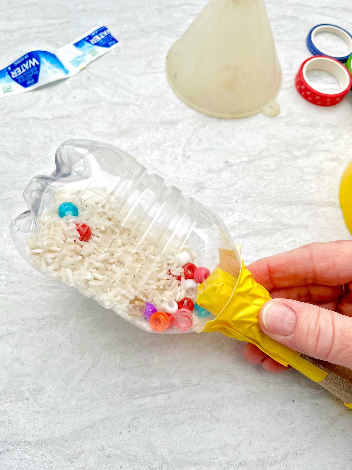 Person holding the water bottle maraca to show dried rice and beads inside.