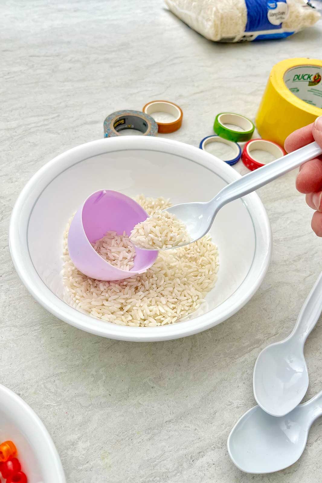 Person filling a purple plastic egg with rice.