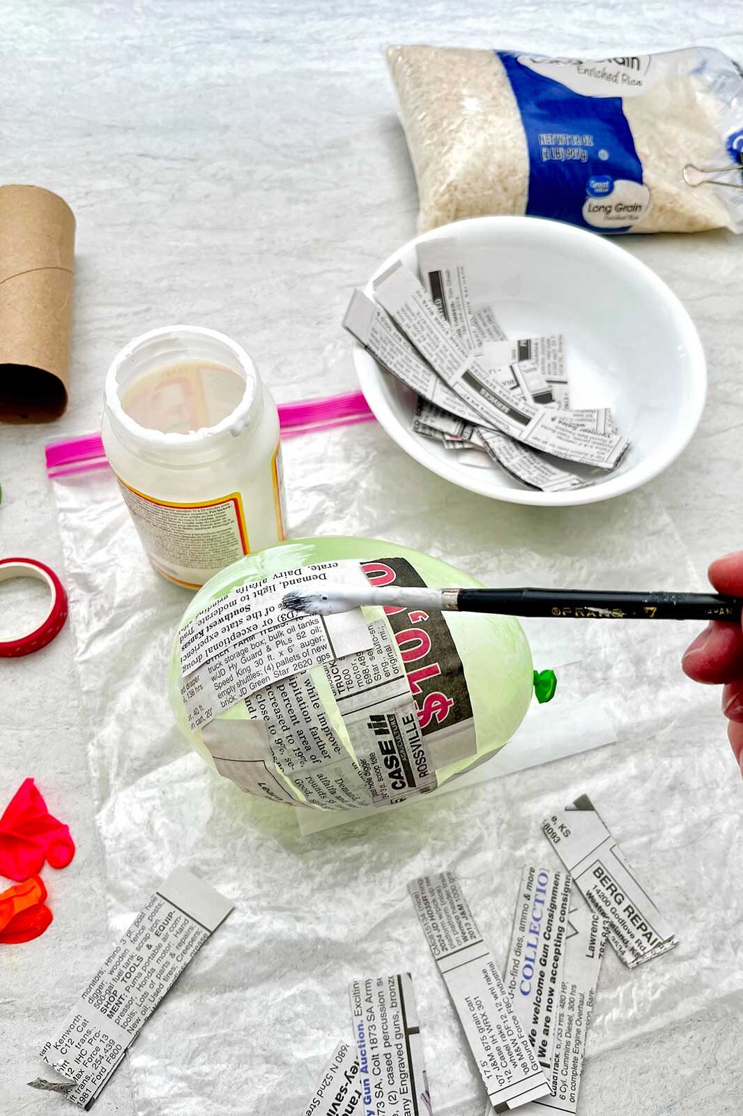 Person painting strips of news paper on to a balloon with mod podge.