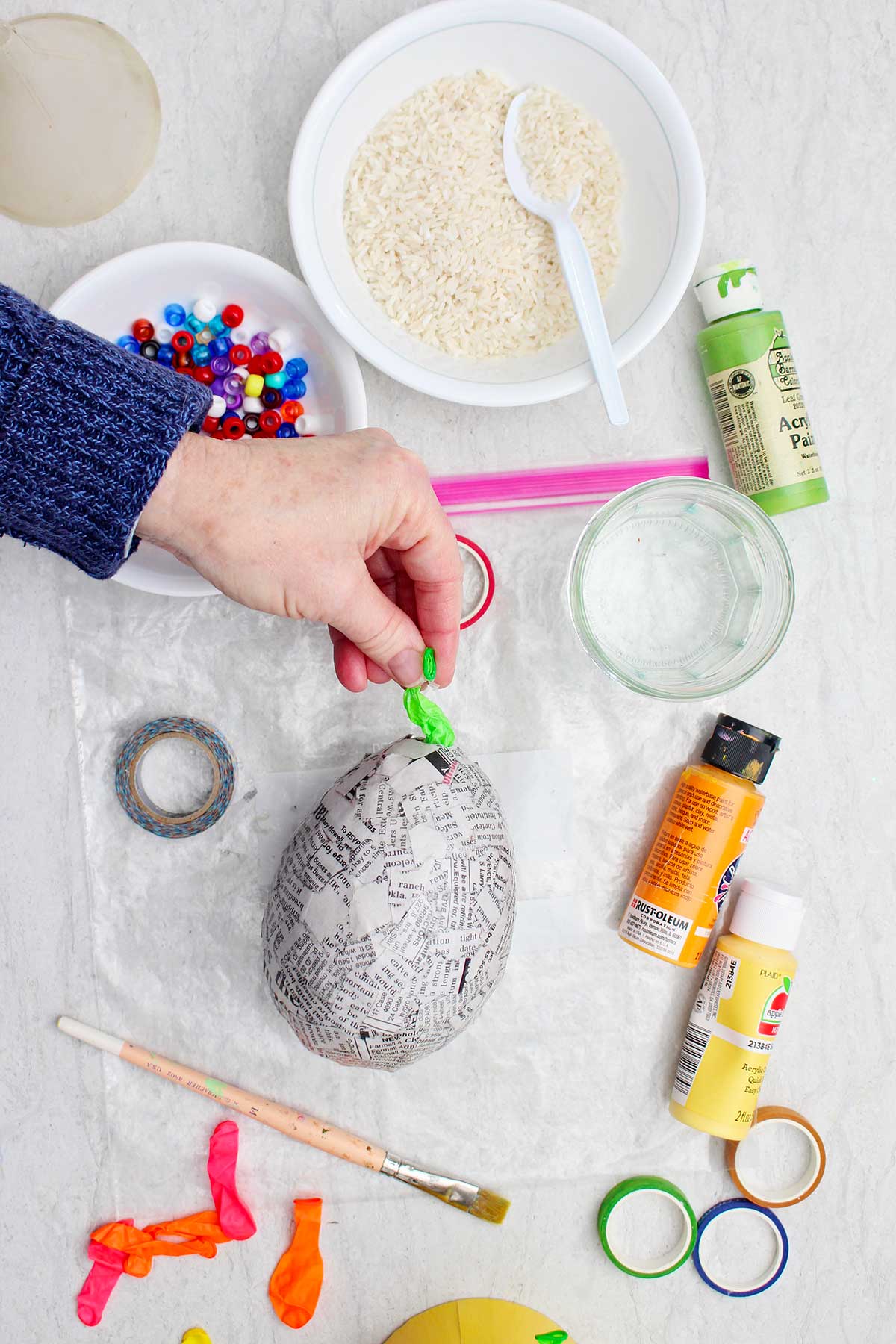 Person removing the popped balloon of a news paper maraca with other supplies near by.