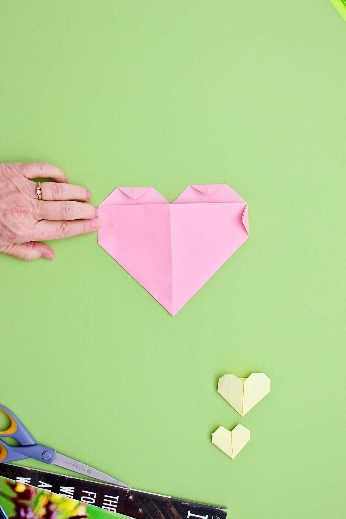 A person folding down the side triangles to complete their origami heart.