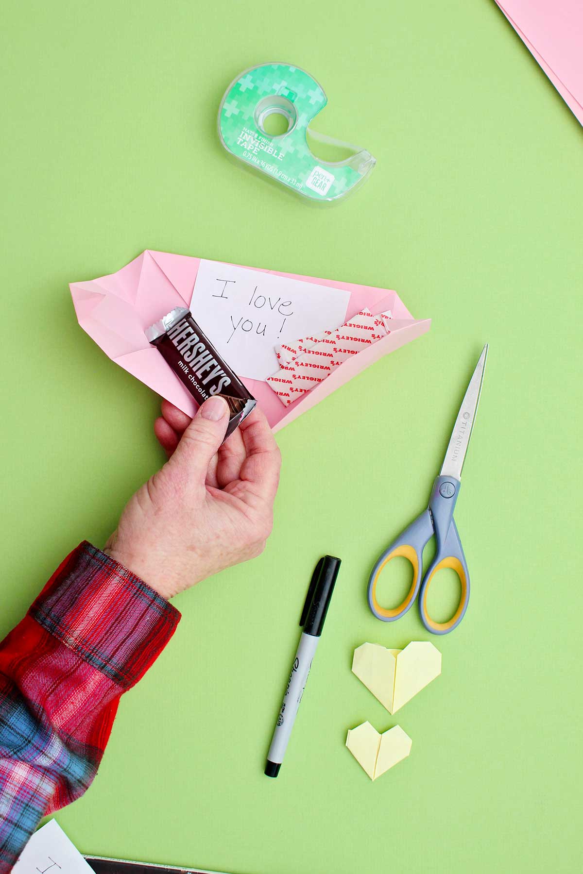 A person placing a small candy bar and a note inside a pink origami heart.