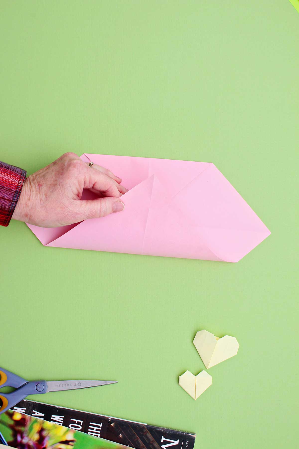 Person folding the corner of a pink piece of paper up to meet the top folded portion.