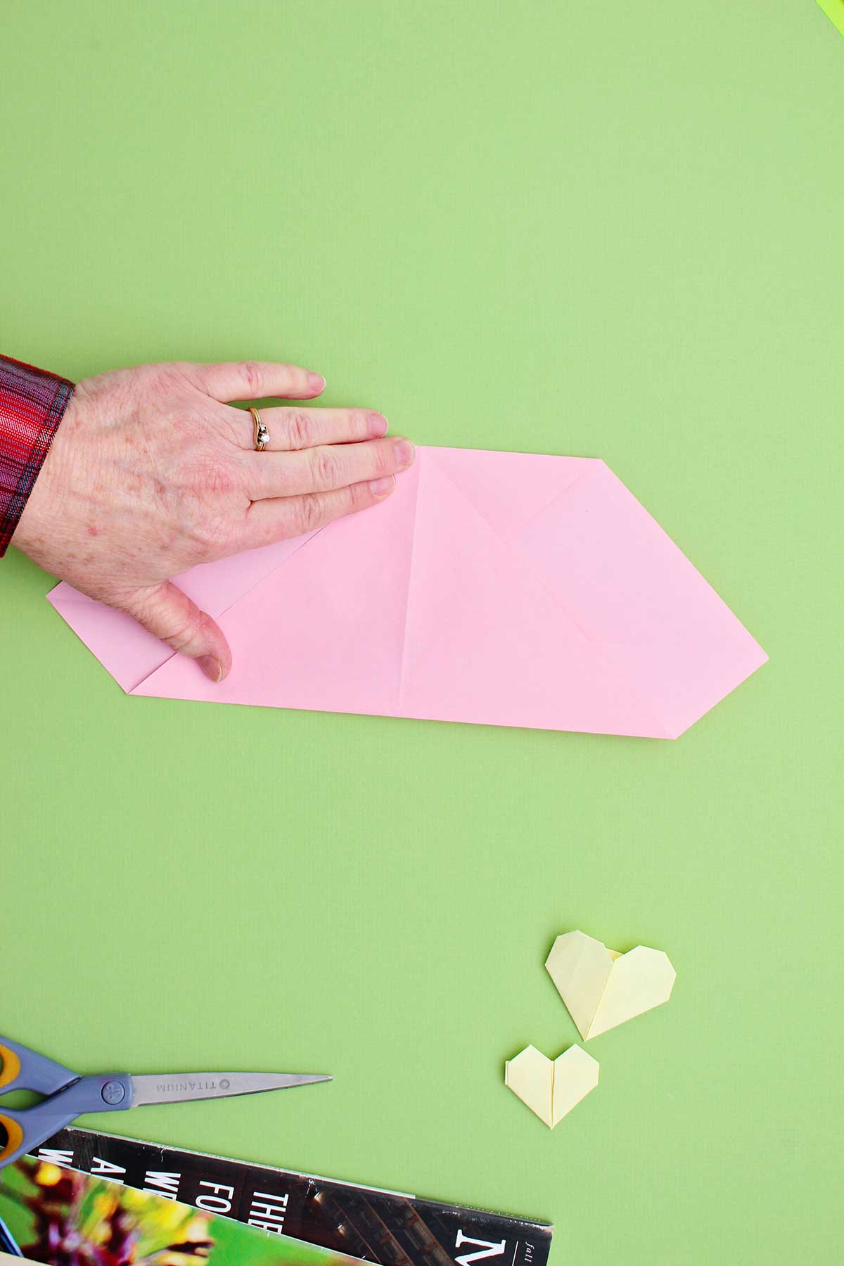 Person folding the corner of a pink piece of paper up to meet the top folded portion.