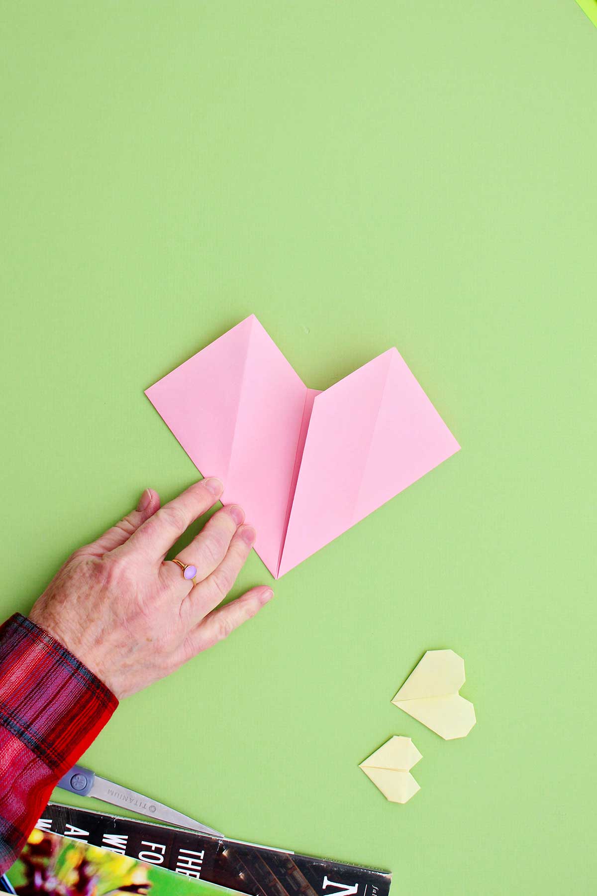 A person folding in the sides to create the body of the origami heart.