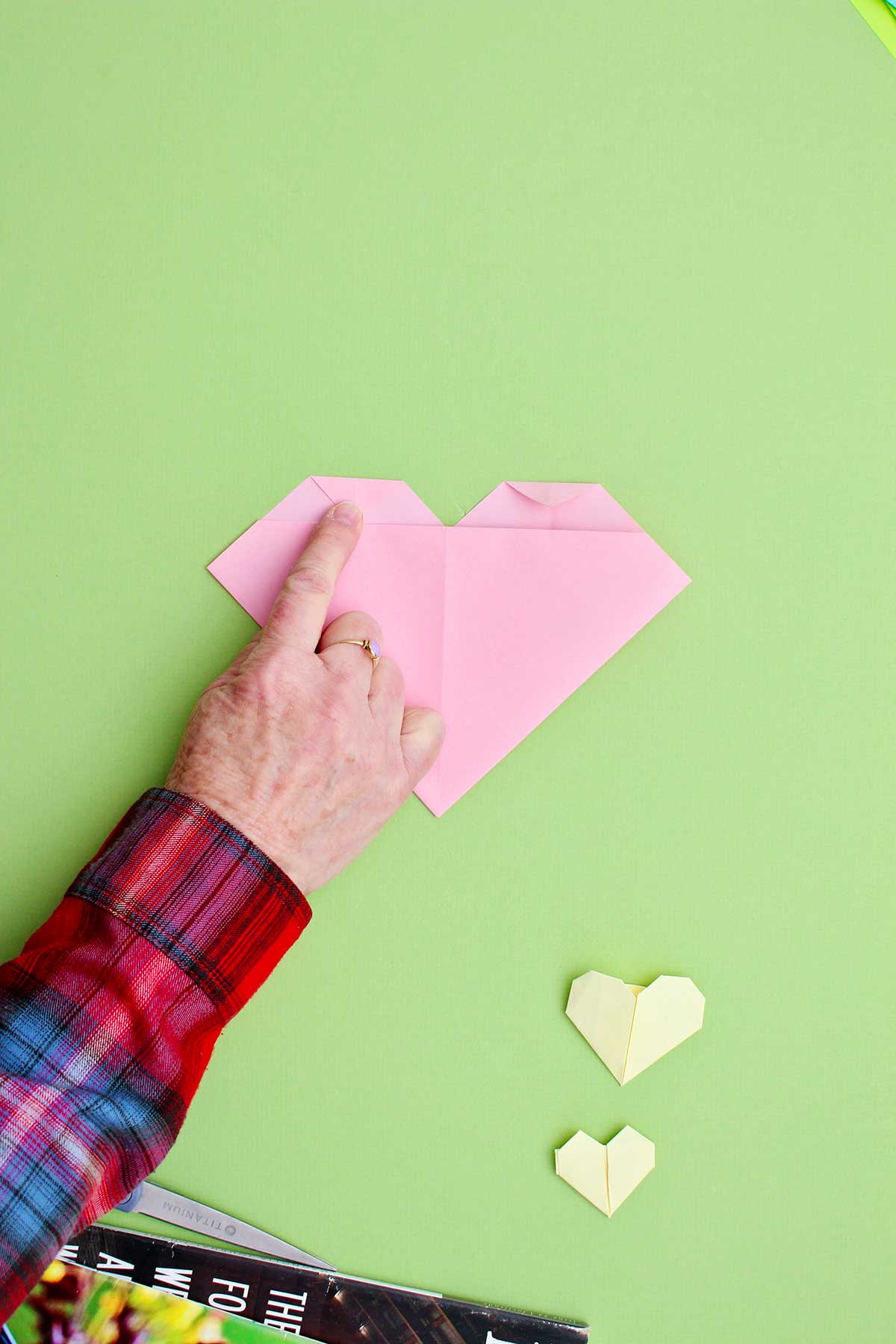 A person folding down small triangles at the top of the origami heart.