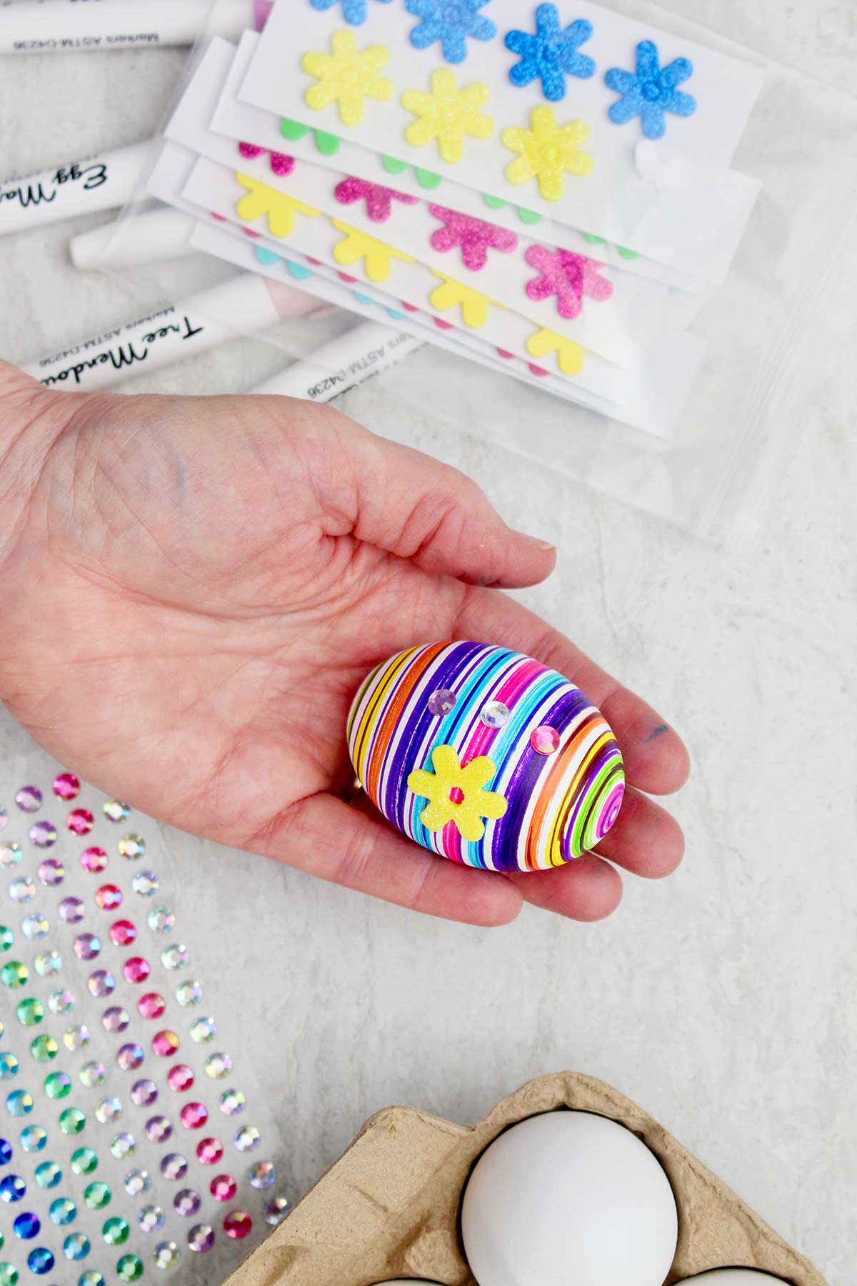 A person holding a fully decorated egg decorated with marker, rhinestones and a yellow flower.