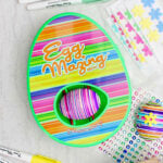 EggMazing striped design kit with striped colored egg inside with other supplies near by.