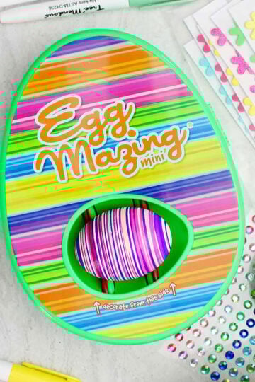 EggMazing striped design kit with striped colored egg inside with other supplies near by.