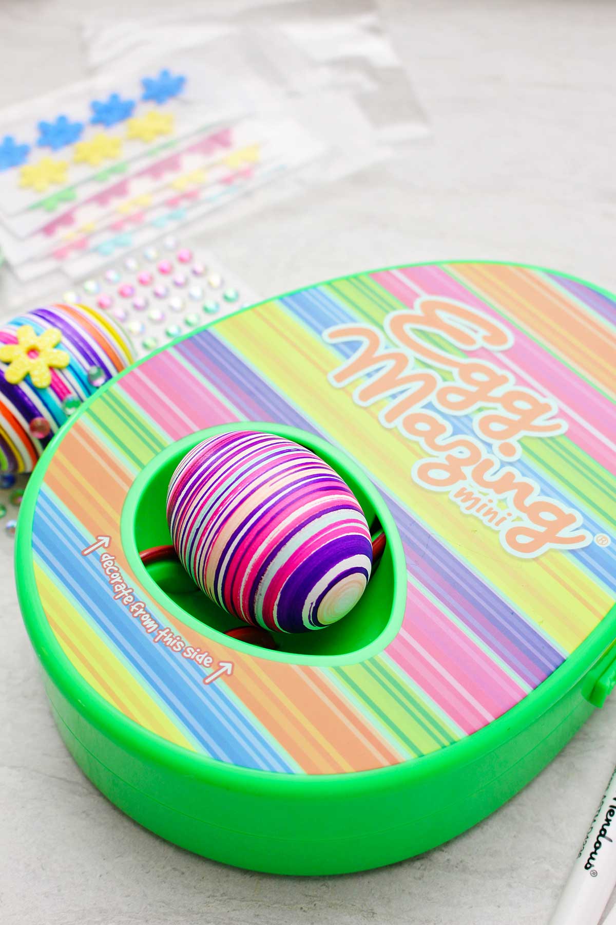 EggMazing striped design kit with striped colored egg inside with other supplies near by.