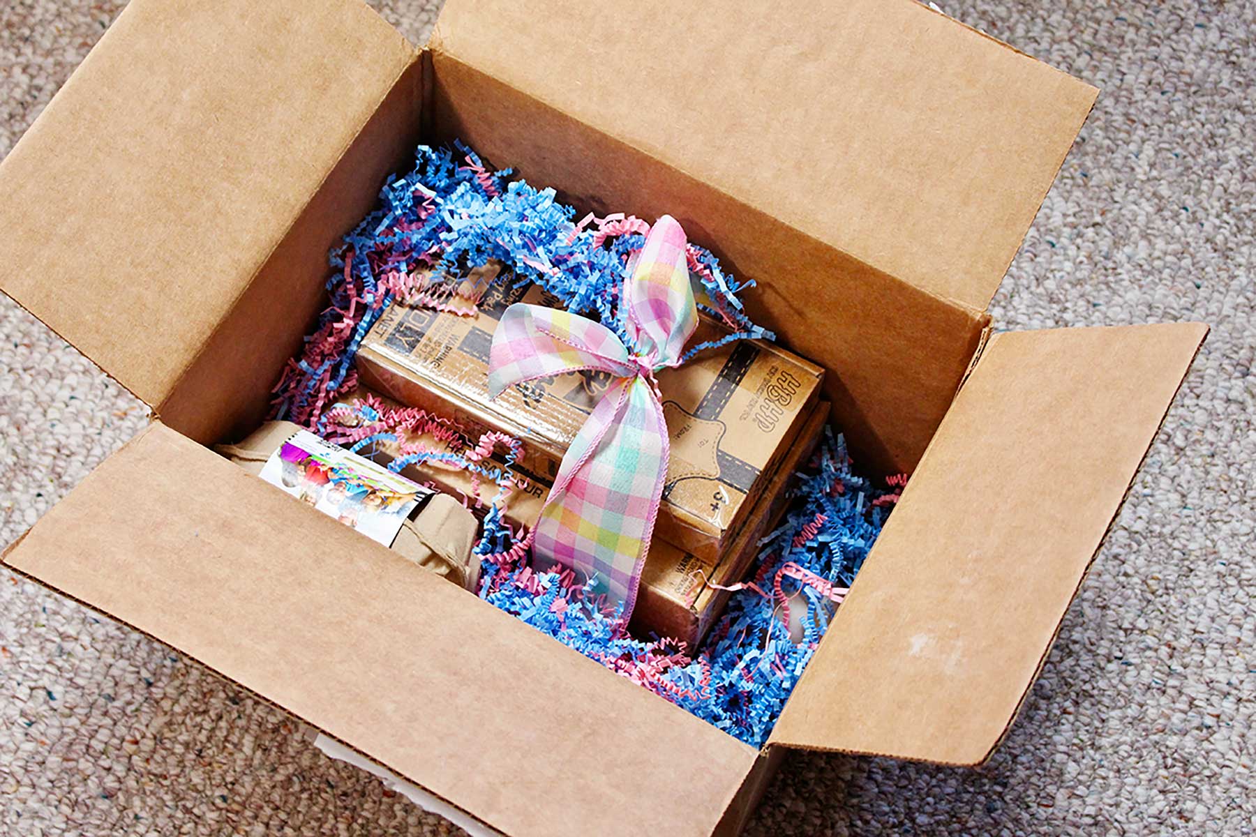 A box full of a gift of EggMazing kits, wooden eggs and easter grass.