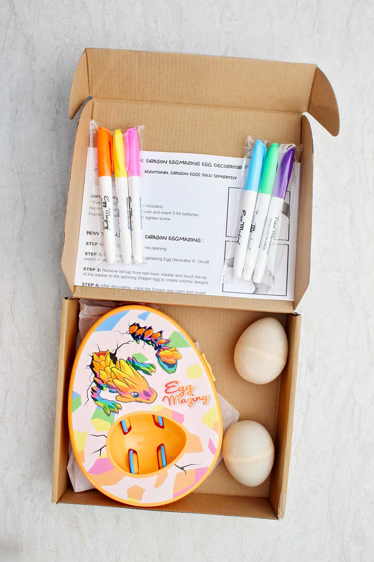 A box full of an EggMazing kit, markers, directions and wooden eggs.