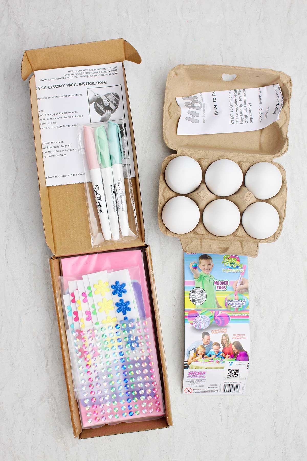 A carton of six wooden eggs, rhinestones, flowers and markers in a box.