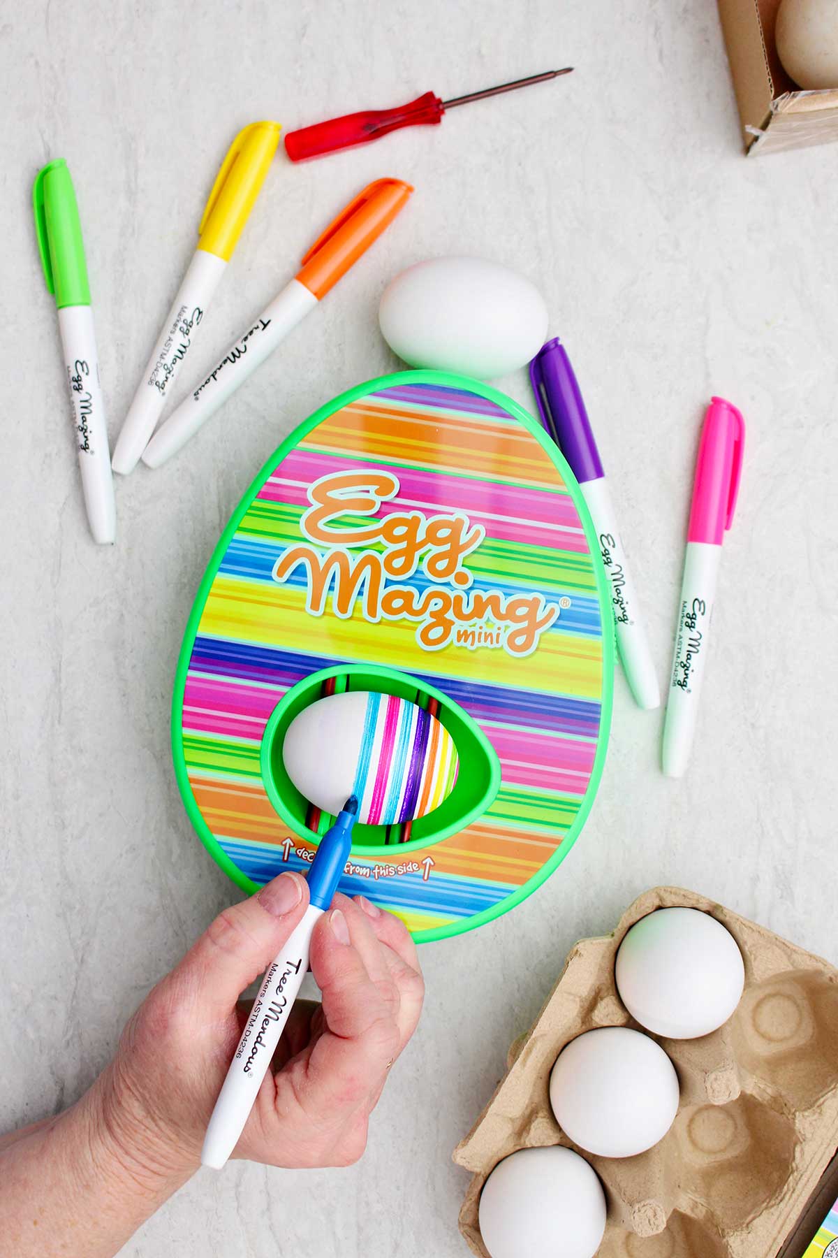 A person using a blue marker to make stripes on the egg in the EggMazing kit.
