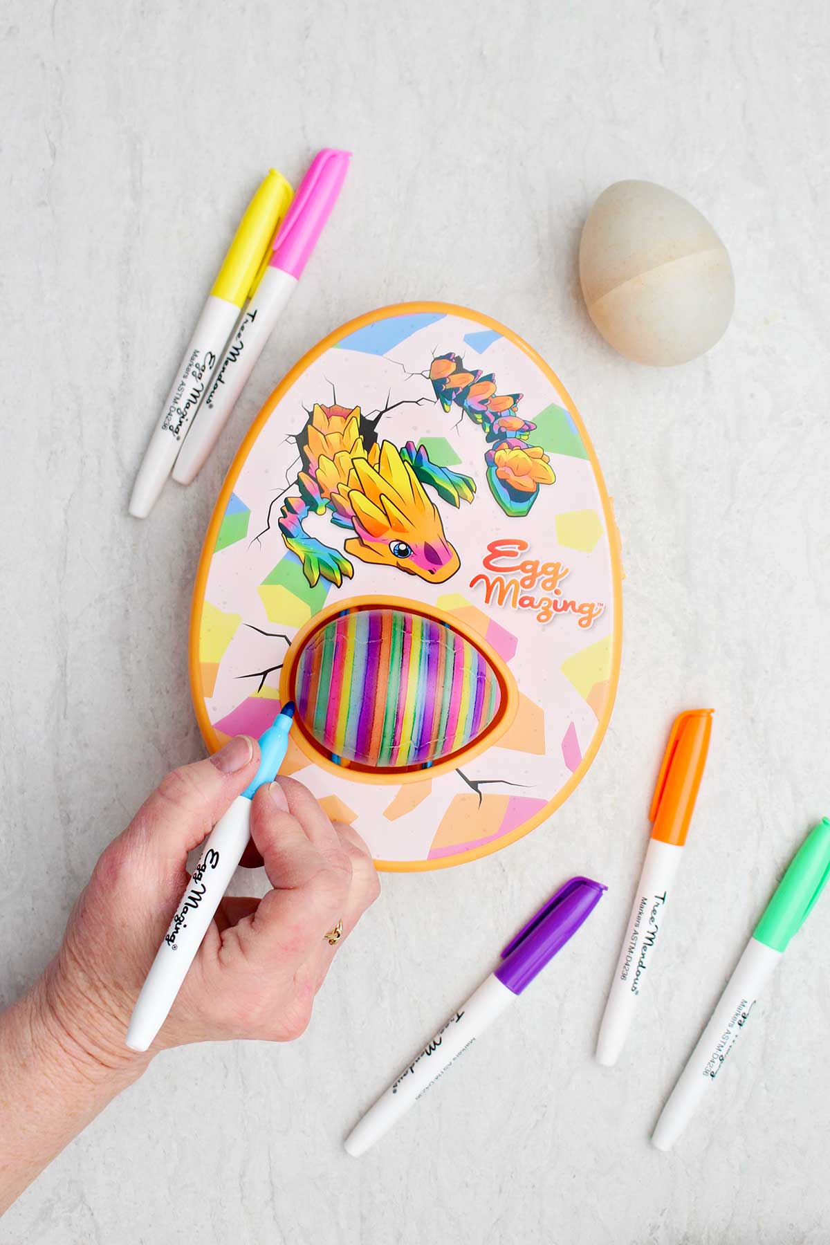 A person using a blue marker on the egg in the EggMazing kit.