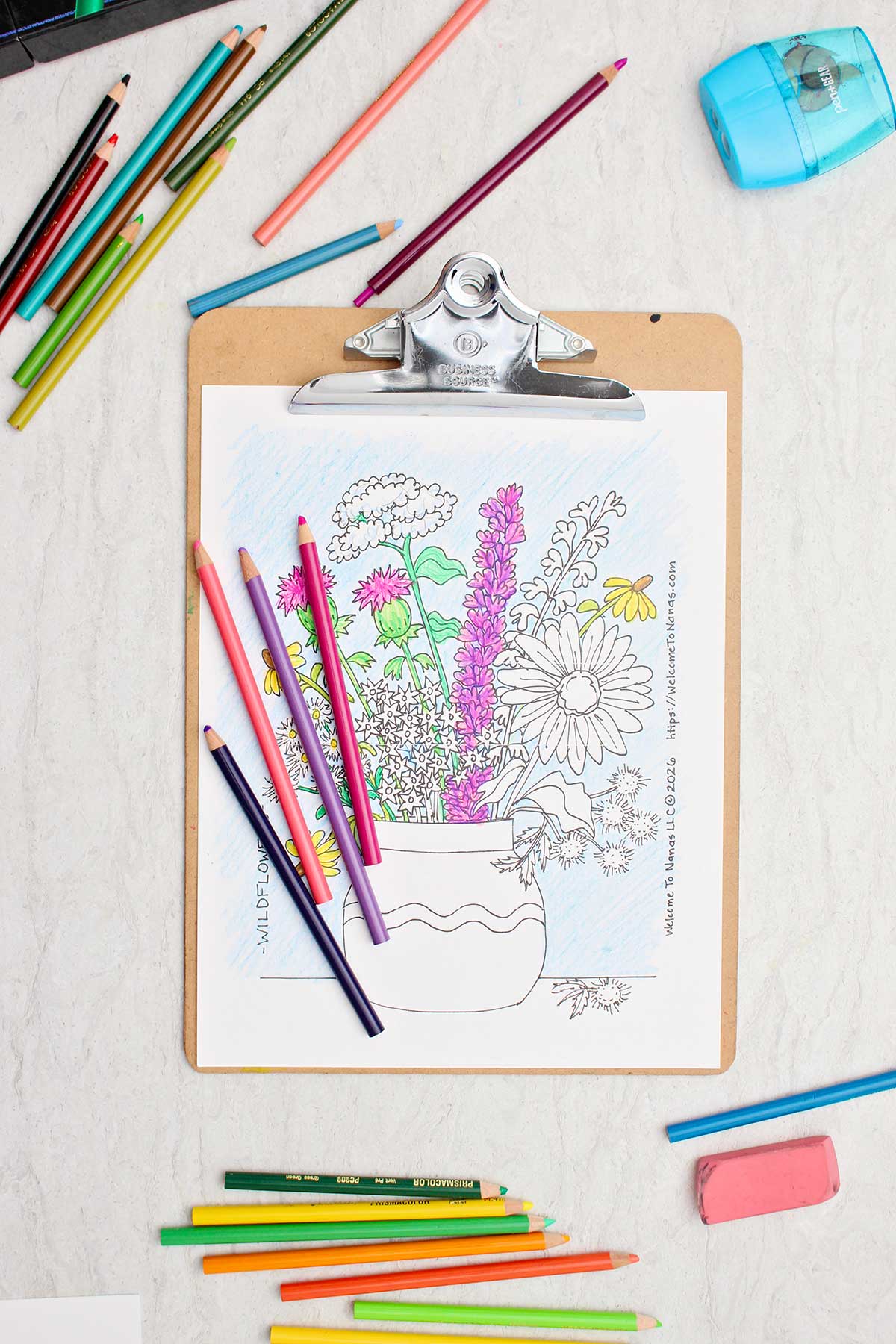 A half completed coloring page of a bunch of wild flowers in a vase with colored pencils near by.