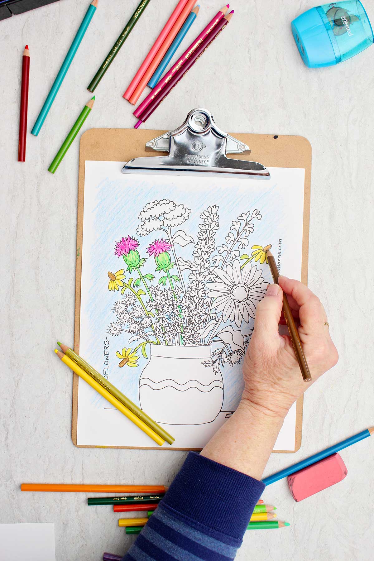 Person coloring a daisy yellow in the coloring page of a bunch of wild flowers in a vase.