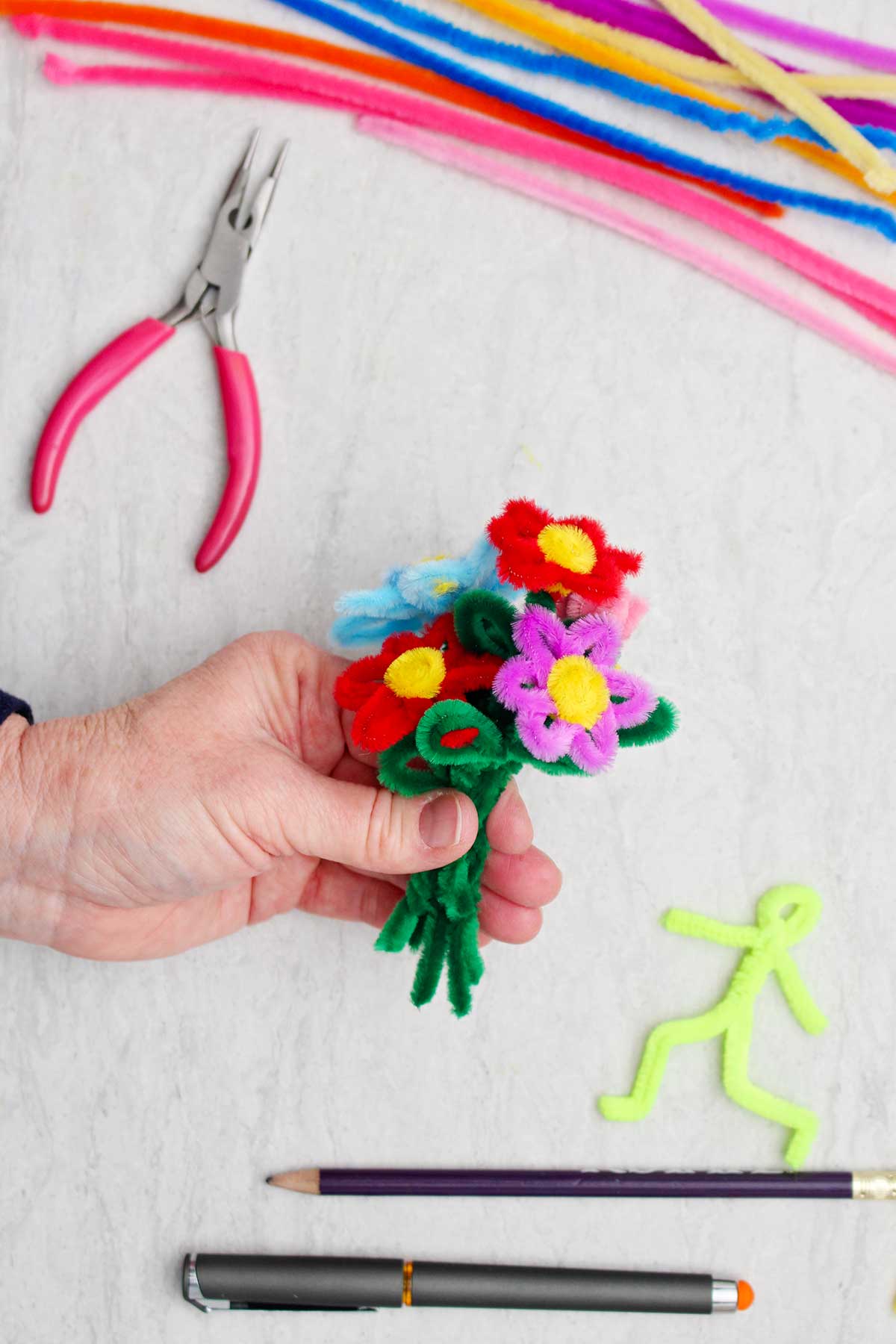A person holding a bouquet of different colored pipe cleaner flowers.