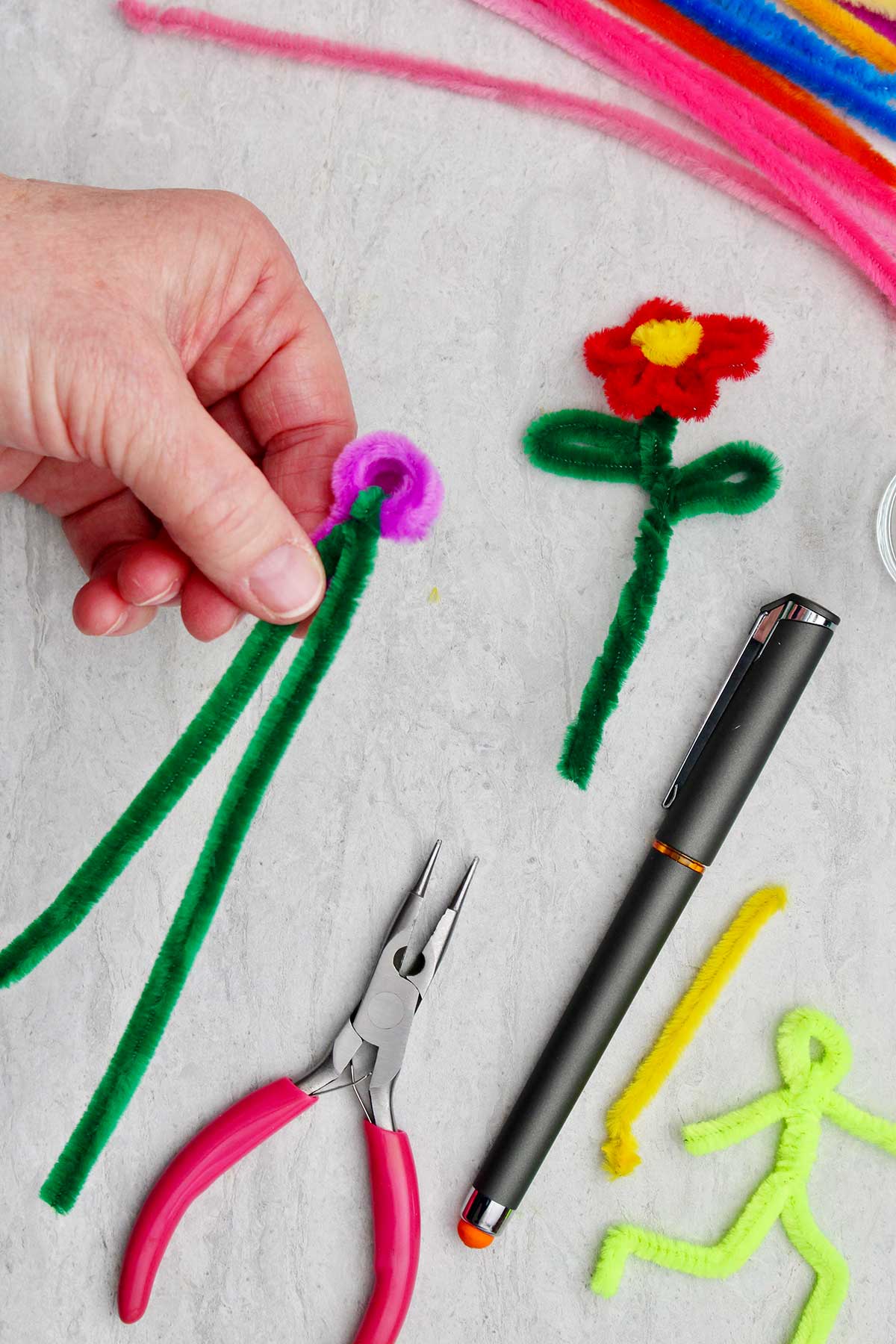 A person holding the start of a pipe cleaner flower with green stem with other supplies near by.
